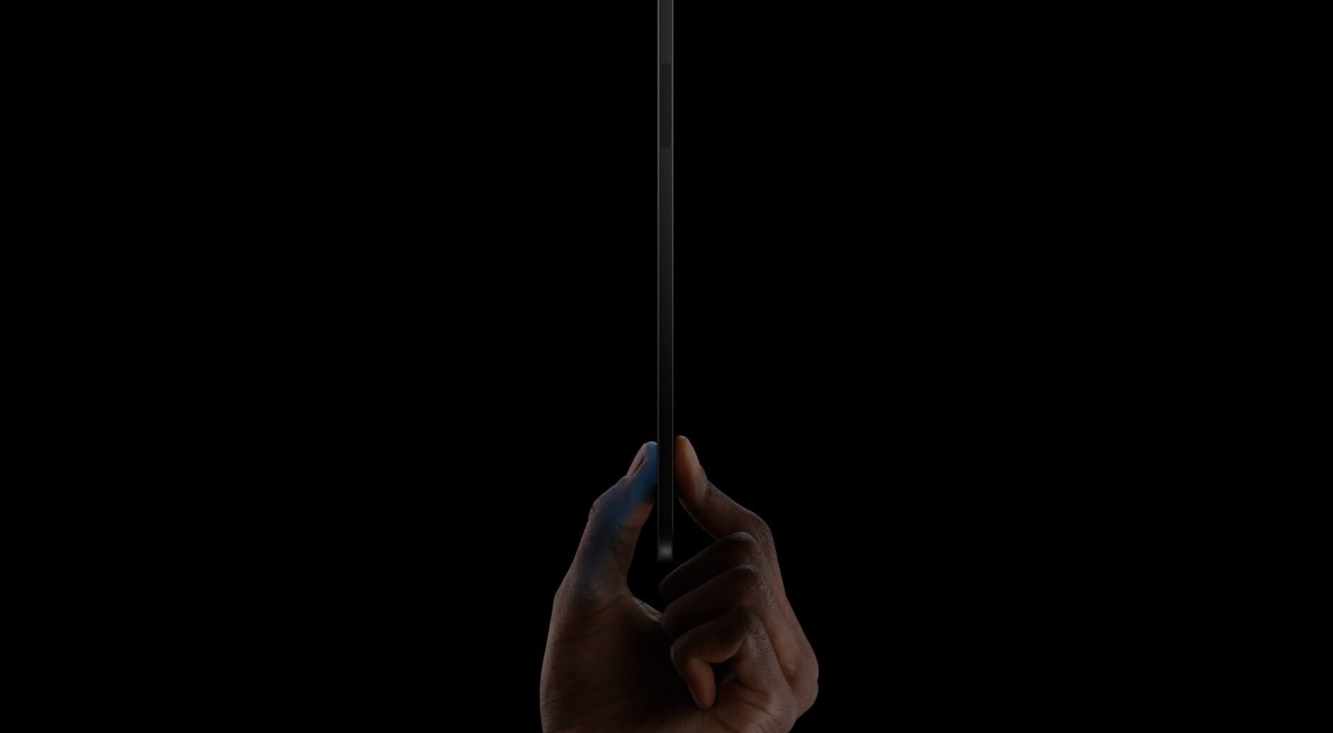 Das Bild zeigt eine Hand, die ein neues iPad Pro zwischen Daumen und Zeigefinger hält, vor einem dunklen Hintergrund.