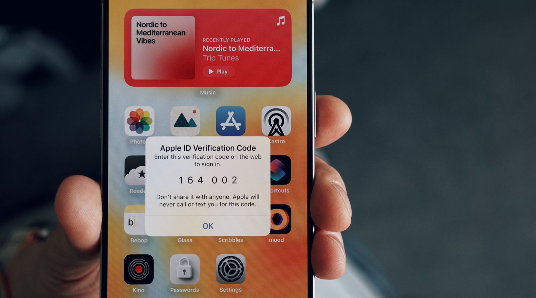 Das Bild zeigt ein iPhone, auf dem ein Apple ID Verifizierungscode angezeigt wird. Der Code lautet "164002" und es wird darauf hingewiesen, diesen Code nicht mit anderen zu teilen.