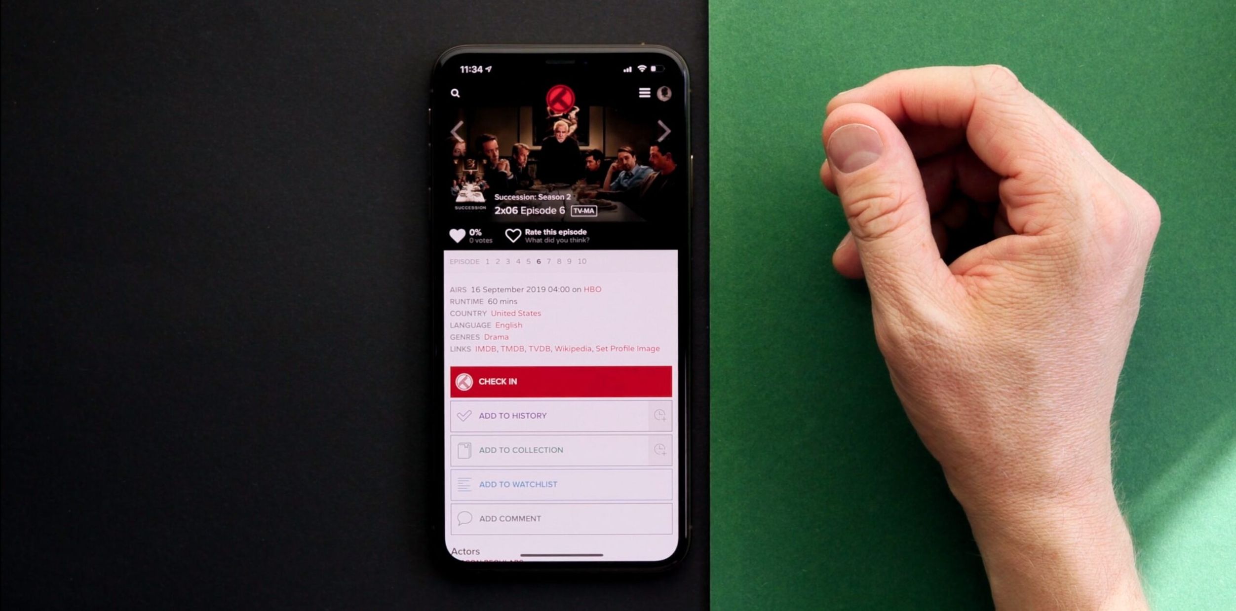 Auf dem Bild ist ein iPhone zu sehen, auf dem Informationen zur sechsten Episode der zweiten Staffel der Serie "Succession" angezeigt werden. Eine Hand befindet sich neben dem Telefon auf einer zweifarbigen Unterlage, die schwarz und grün ist.