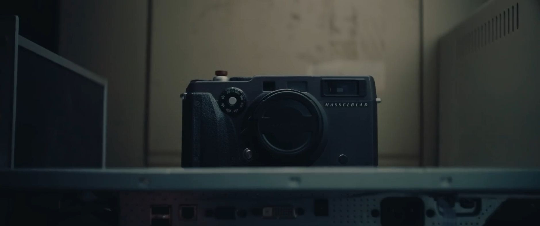 Das Bild zeigt eine Hasselblad-Kamera, die in einem Regal oder Schrank platziert ist. Die Kamera ist zentral positioniert und von einem dunklen, neutralen Hintergrund umgeben. Der Schriftzug "Hasselblad" ist deutlich auf der Vorderseite der Kamera zu erkennen.