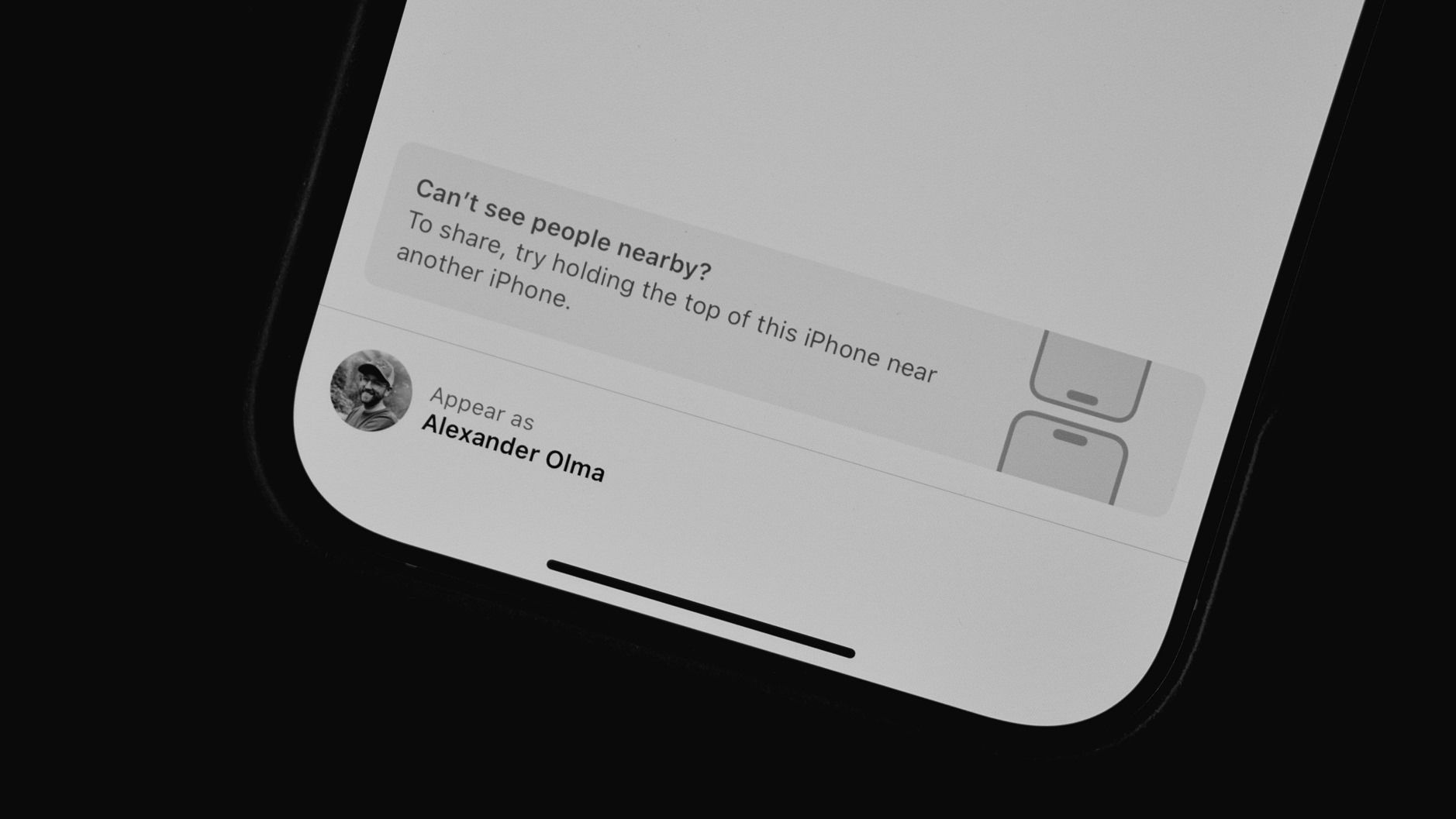 Das Bild zeigt die Benutzeroberfläche eines iPhones, auf dem eine Funktion zum Teilen von Informationen mit Personen in der Nähe angezeigt wird. Es gibt einen Hinweis, dass man die Oberseite des iPhones nahe an ein anderes Gerät halten soll, falls keine Personen sichtbar sind. Unten sieht man ein Profilbild und den Namen "Alexander Olma", unter dem der Nutzer erscheint.