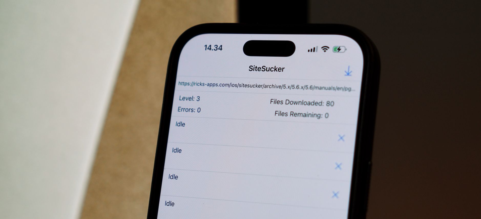 Das Bild zeigt ein iPhone, auf dem die App "SiteSucker" geöffnet ist. Die App wird verwendet, um Webseiten zu kopieren, und zeigt Informationen wie die Anzahl der heruntergeladenen Dateien (80) und verbleibende Dateien (0). Die Benutzeroberfläche ist minimalistisch und zeigt den Status als "Idle" (Leerlauf).
