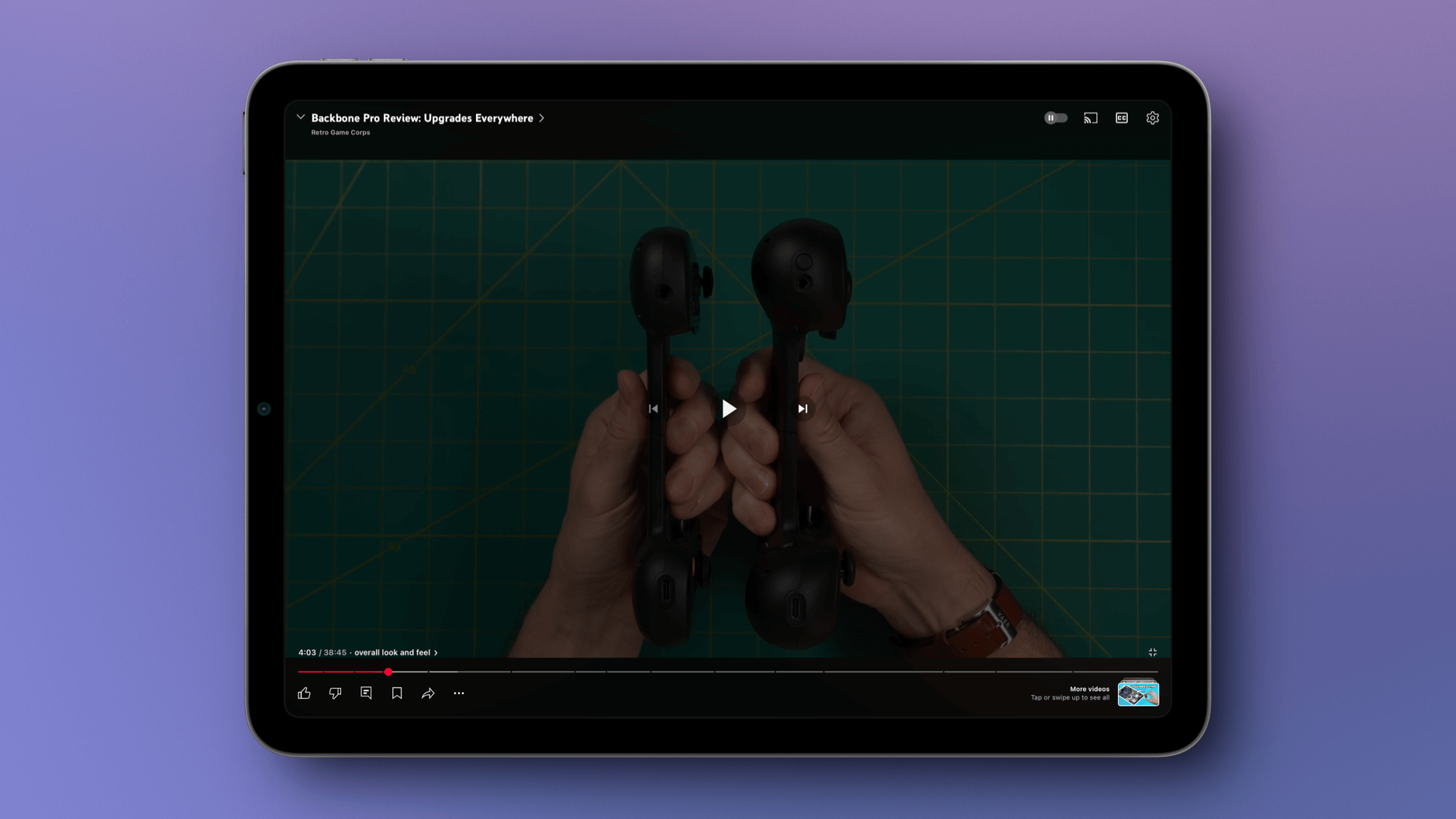 Das Bild zeigt ein Tablet, auf dem ein Video über den Backbone Pro Controller angezeigt wird, mit dem Titel "Backbone Pro Review: Upgrades Everywhere". Im Video sind zwei schwarze Gaming-Controller zu sehen, die von Händen gehalten werden, vor einem grünen Hintergrund mit Rasterlinien. Der Videoplayer zeigt, dass das Video bei 4:03 von insgesamt 38:45 Minuten ist, mit der Beschreibung "overall look and feel".