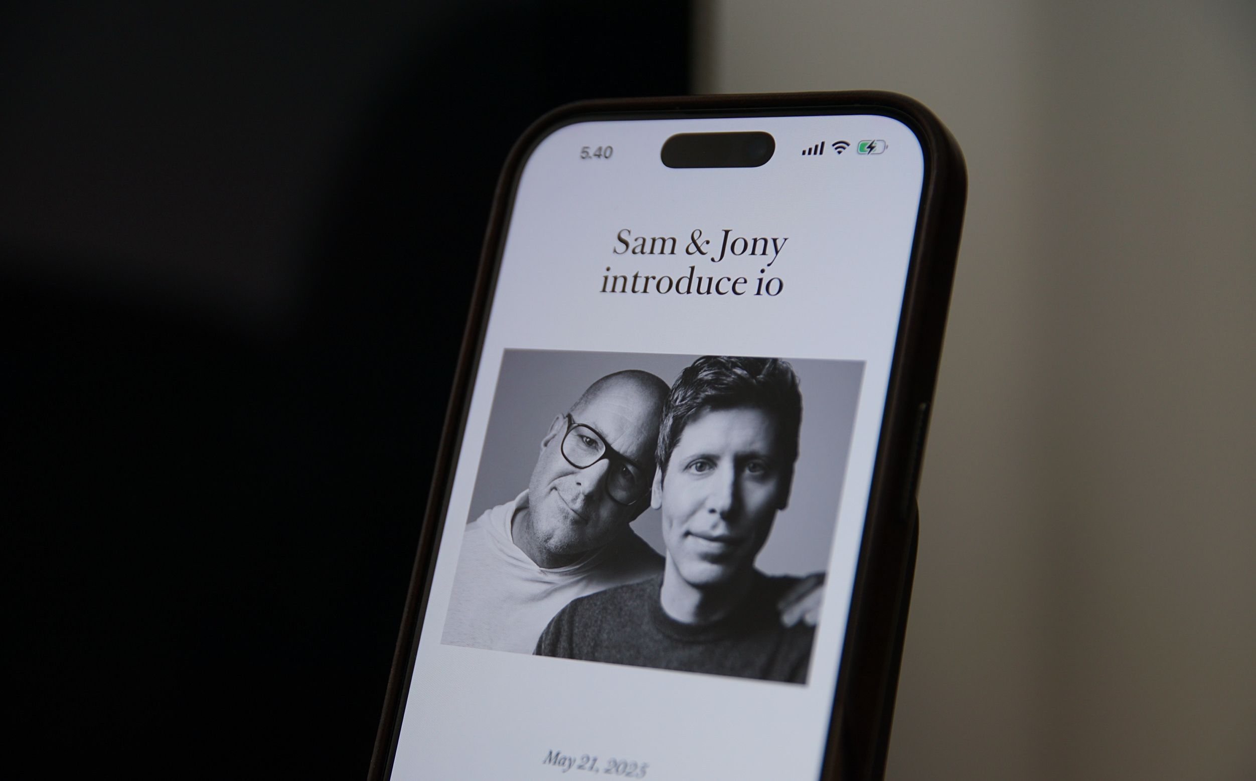 Das Bild zeigt einen Smartphone-Bildschirm mit dem Text "Sam & Jony introduce io" und einem schwarz-weißen Porträt von zwei Personen. Es ist der 21. Mai 2023 vermerkt. Die Darstellung wirkt modern und minimalistisch.