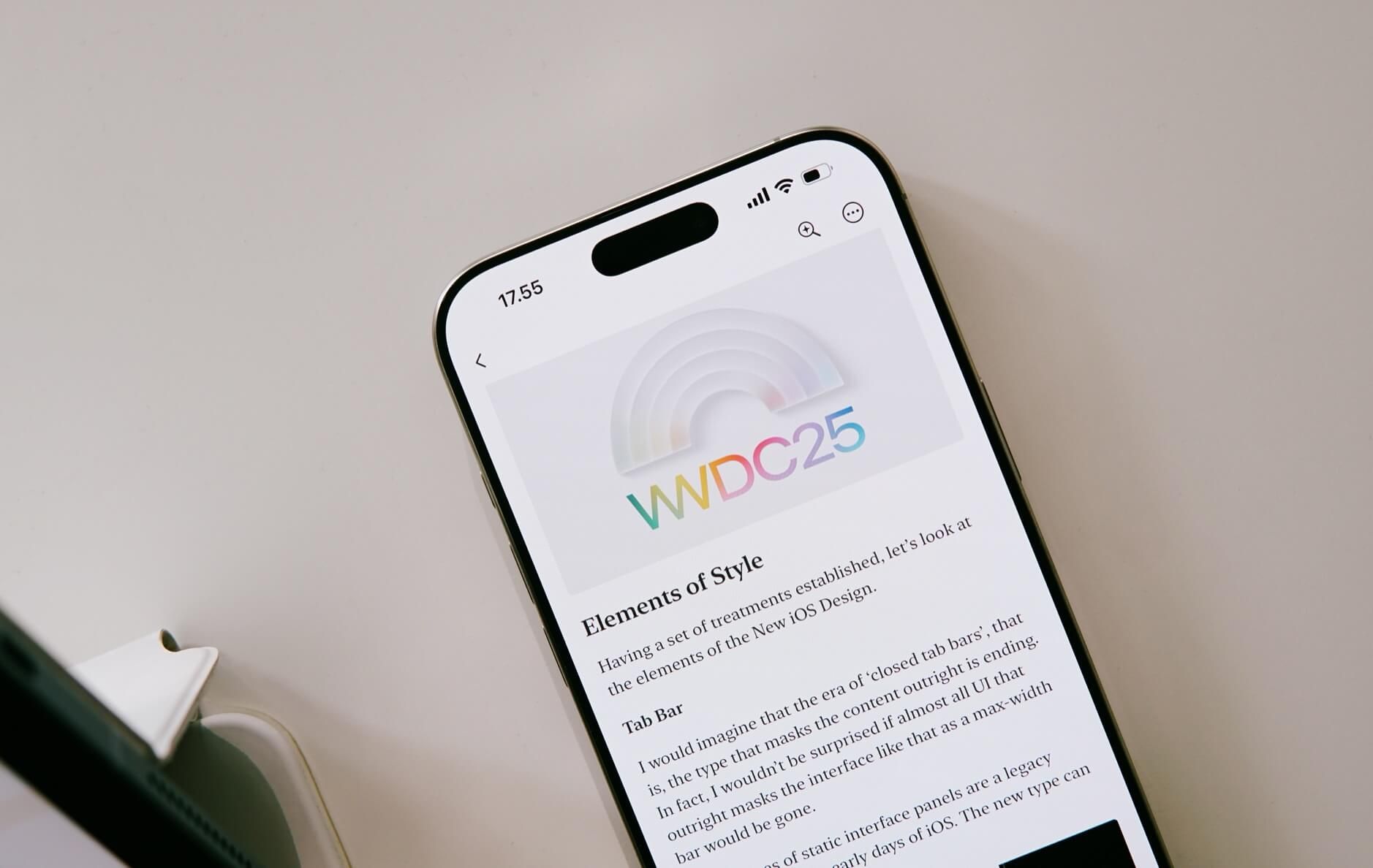 Auf dem Bild ist ein Smartphone zu sehen, das eine Webseite mit dem WWDC25-Logo anzeigt. Unter dem Logo steht die Überschrift „Elements of Style“ und ein Text über das neue iOS-Design. Das Gerät liegt auf einer hellen Oberfläche.