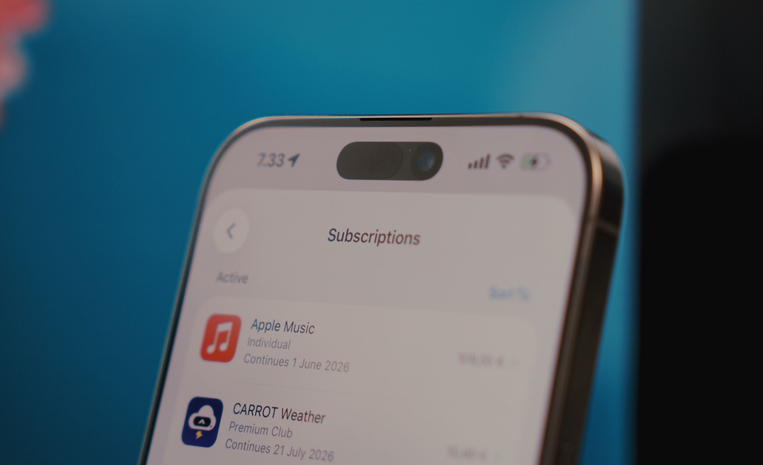 Close-up of an iPhone screen displaying the "Subscriptions" section within the App Store, with Apple Music and CARROT Weather subscriptions visible, the time, and the phone's status bar.