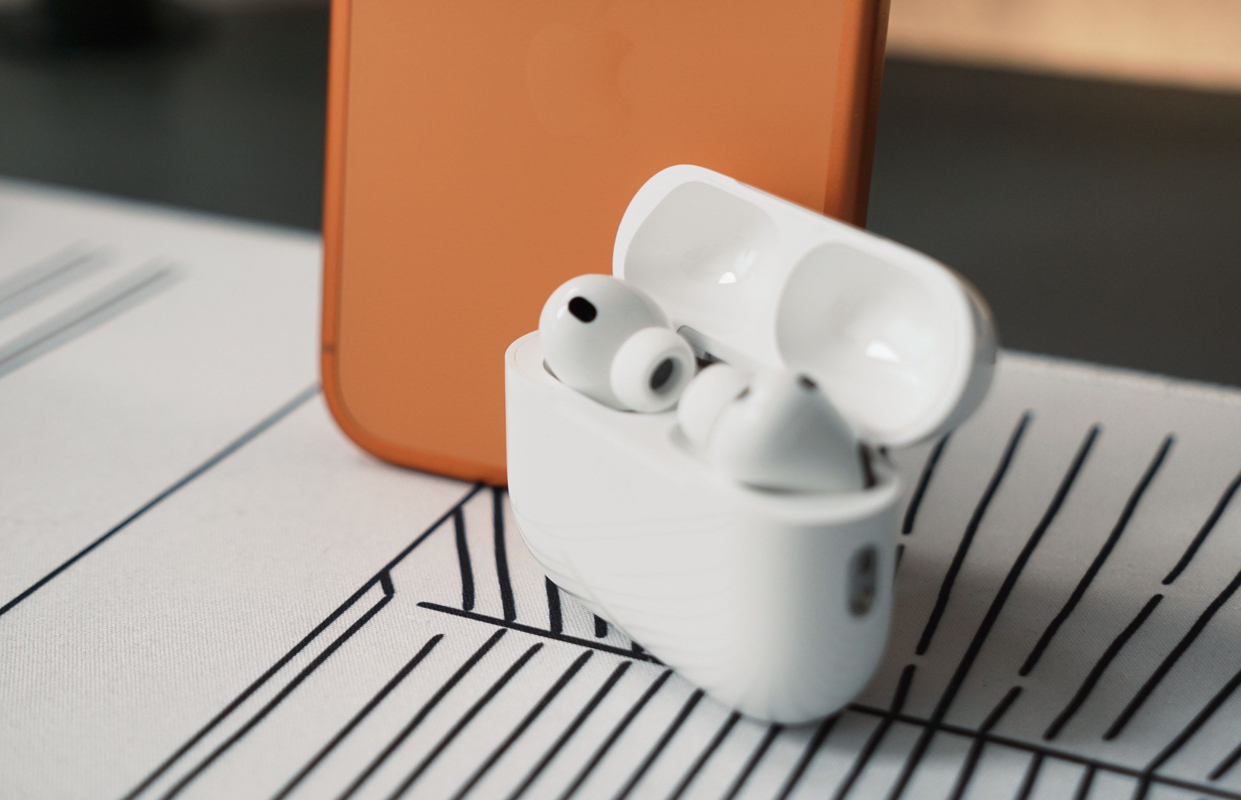 White wireless earbuds with charging case and phone on a patterned white surface.
