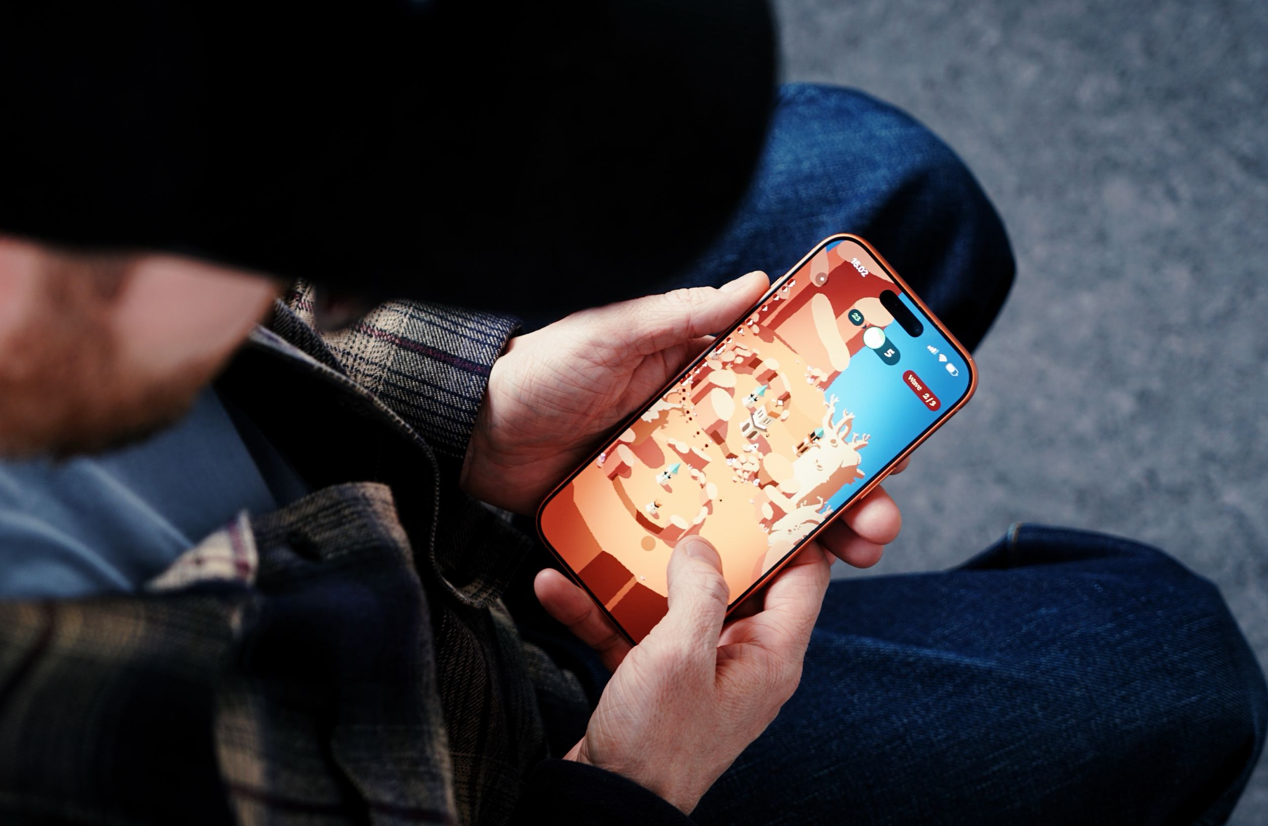 Person hält ein orangefarbenes Smartphone, das ein farbenfrohes, abstraktes Handyspiel auf blauem und orangefarbenem Hintergrund anzeigt, vor einem verschwommenen Hintergrund aus Torso und Beinen einer Person.