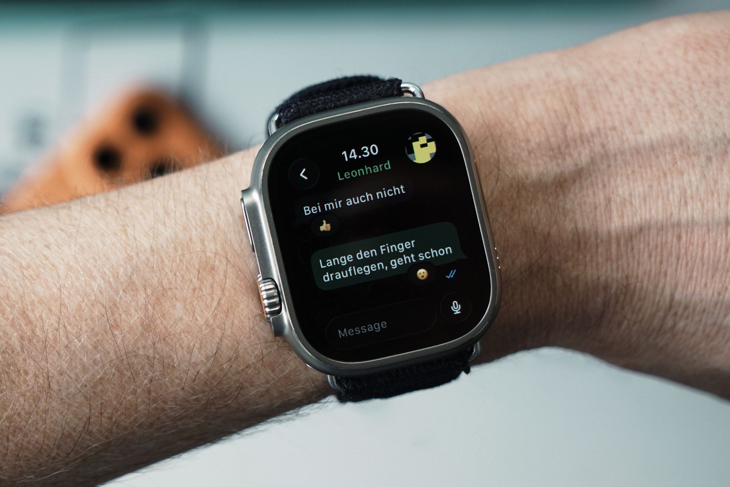 A close-up of a wrist with a silver smartwatch displaying a messaging app. The time on the watch reads "14.30" and the sender is "Leonhard." The message threads say: "Bei mir auch nicht" and "Lange den Finger drauflegen, geht schon."