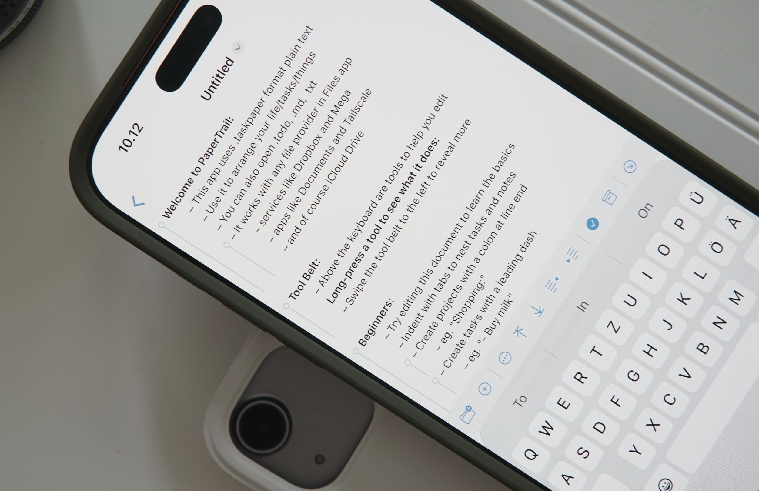 Eine Nahaufnahme eines Smartphone-Bildschirms, auf dem die App „PaperTrail“ geöffnet ist. Das Display zeigt eine Willkommensnachricht und Anweisungen zur Verwendung der App für die Organisation von Aufgaben und Notizen im Klartextformat. Am unteren Bildschirmrand ist eine virtuelle Tastatur zu sehen.