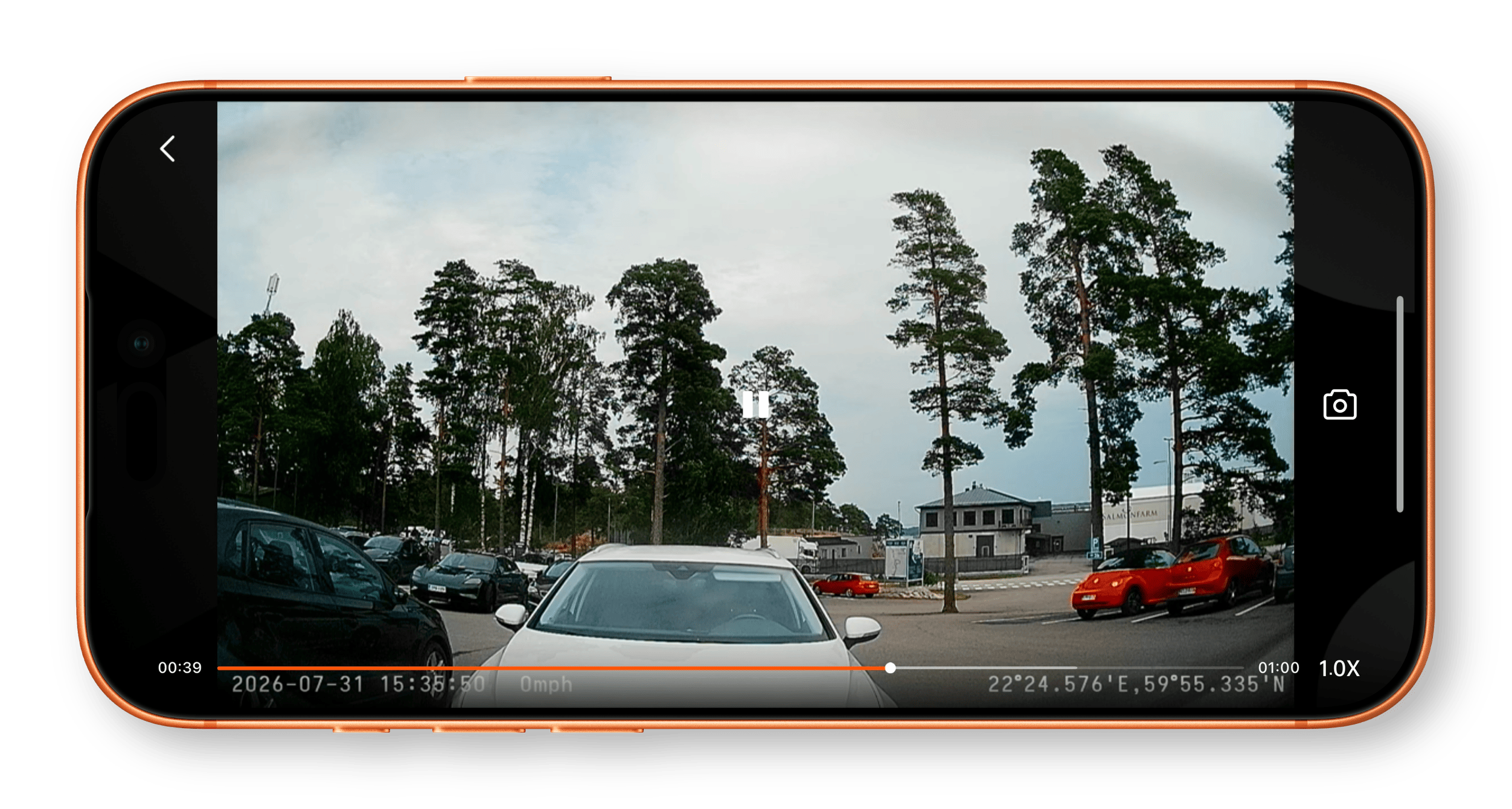 Ein Smartphone-Display zeigt eine Dashcam-Aufnahme eines Parkplatzes mit Autos, Bäumen und einem Gebäude, ergänzt durch Einblendungen von Zeitstempel, Geschwindigkeit und GPS-Daten.