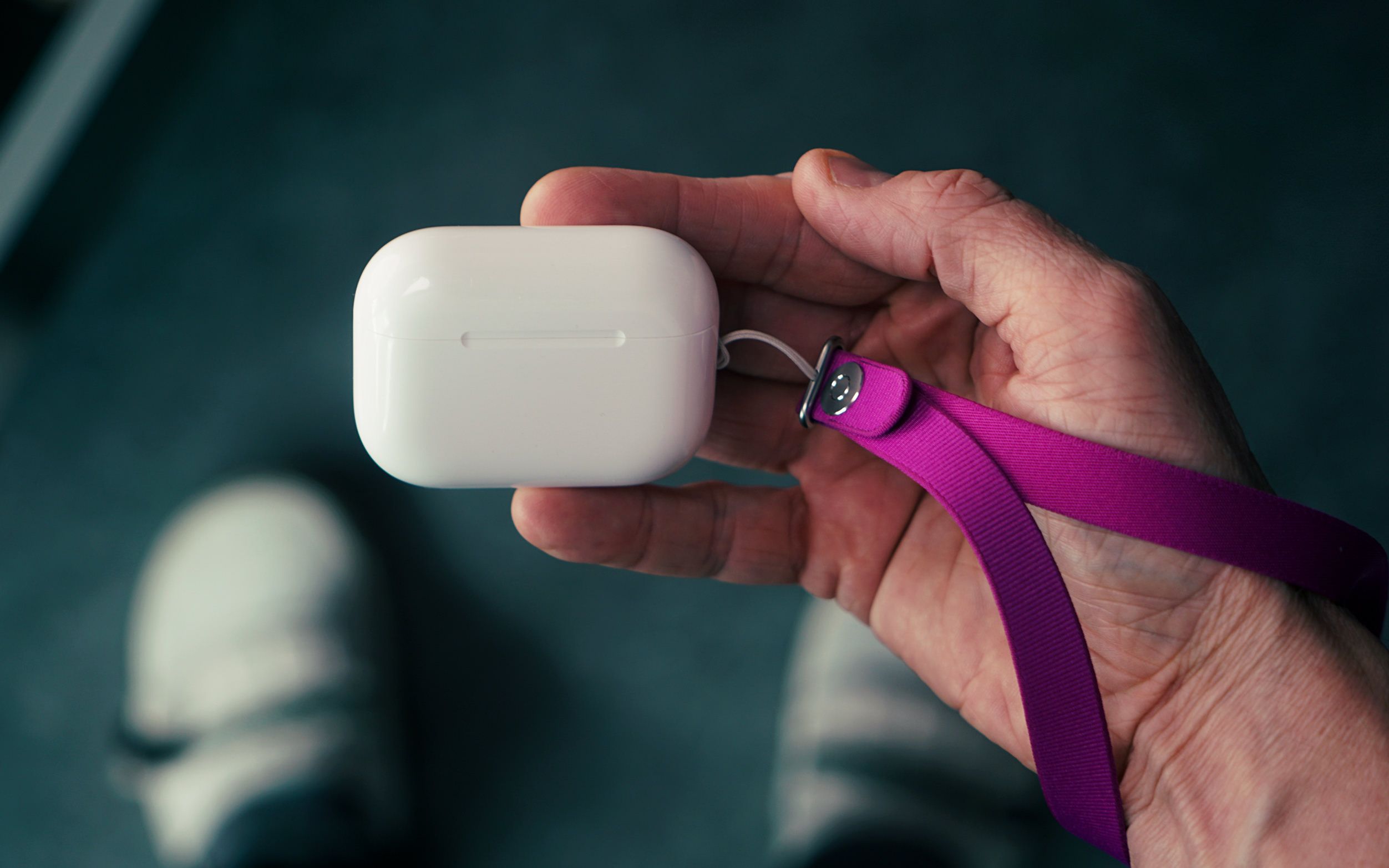 A person's hand holding a white earbud charging case attached to a purple lanyard.
