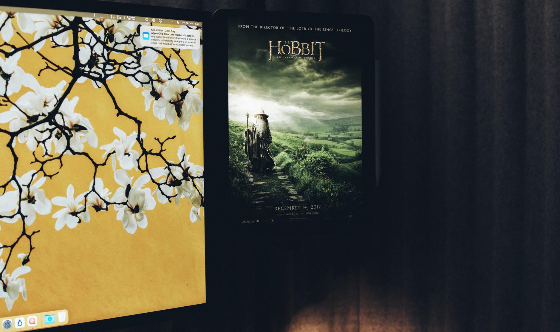 Das Bild zeigt einen Computerbildschirm mit einem blumigen Hintergrundbild neben einem Tablet, auf dem ein Filmplakat von "Der Hobbit: Eine unerwartete Reise" zu sehen ist. Das Tablet lehnt an einer dunklen Vorhangseite und der Film wird am 14. Dezember 2012 veröffentlicht.