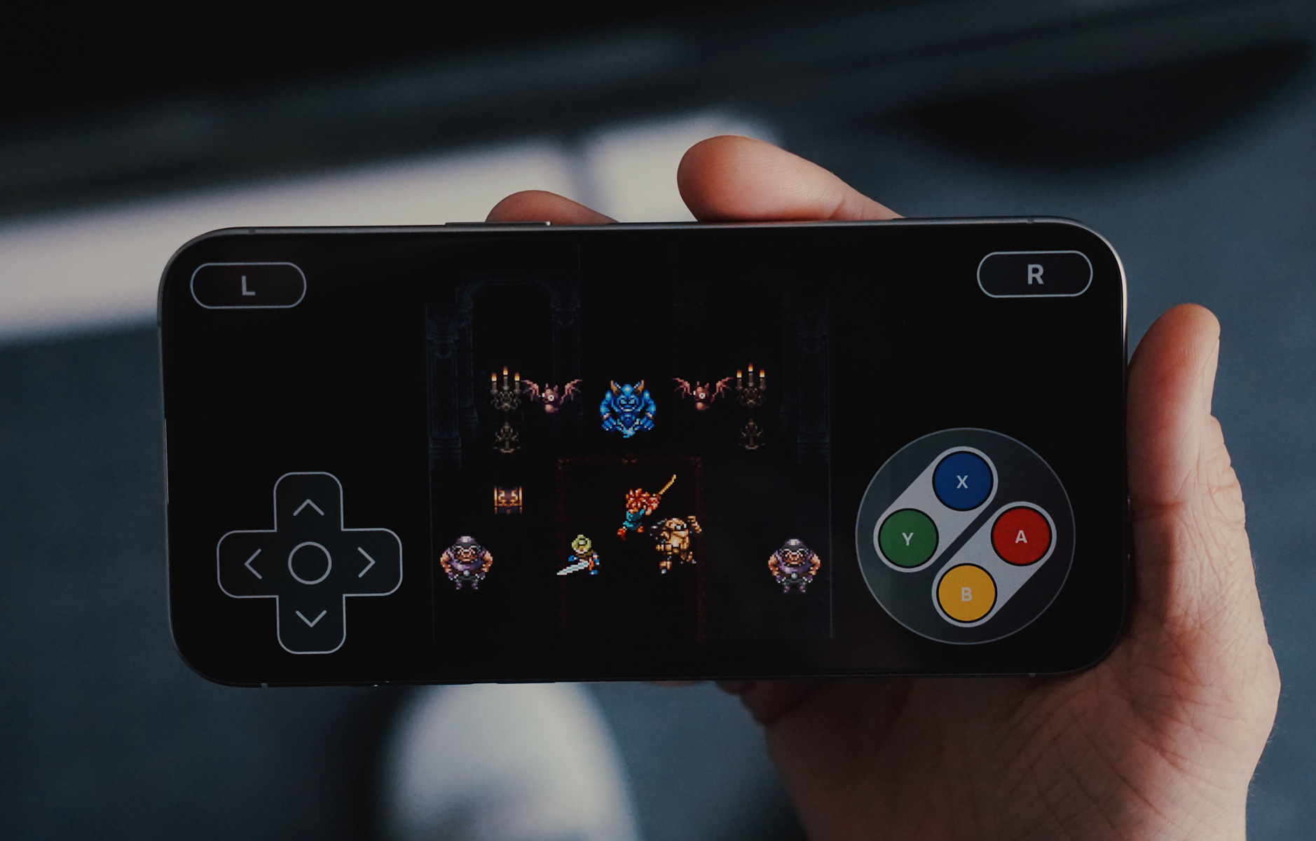 Das ist ein Bild von einer Hand, die ein Smartphone hält, auf dessen Bildschirm ein Retro-Videospiel mit Pixelgrafik läuft. Auf dem Bildschirm sind Spielelemente zu sehen, darunter eine Spielfigur mit einem Schwert, Gegner und ein virtuelles Gamepad mit Tasten.