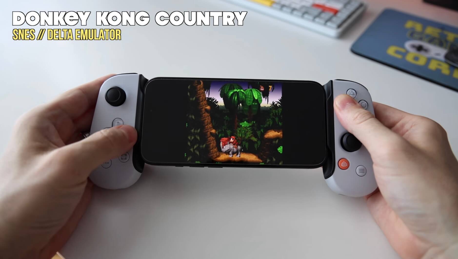 Das Bild zeigt zwei Hände, die ein Smartphone halten, auf dem das Spiel "Donkey Kong Country" über einen SNES-Emulator namens Delta gespielt wird. Die Hände bedienen auch einen an das Telefon angeschlossenen Gamecontroller.