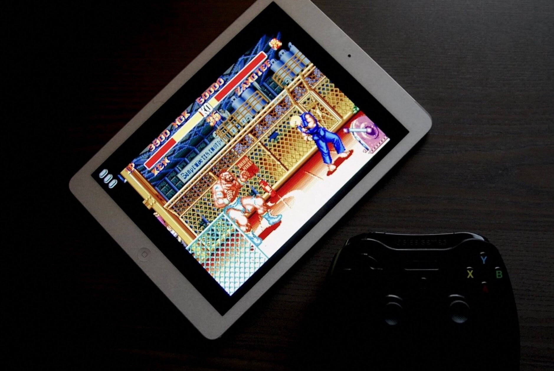 Das Bild zeigt ein iPad, auf dem Street Fighter läuft, und einen Controller, der davor auf einem Tisch liegt. Es sieht so aus, als ob jemand bereit ist, das Spiel mit dem Controller zu spielen.