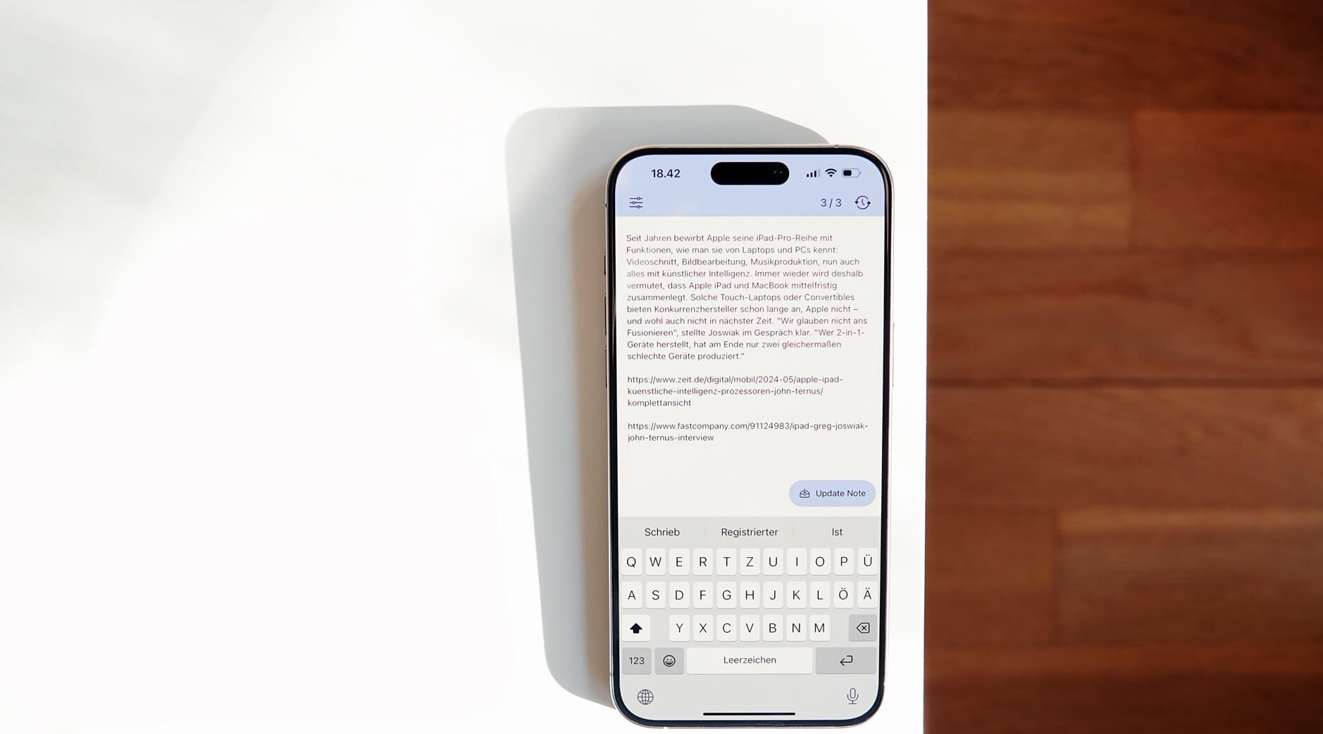 Das Bild zeigt ein modernes Smartphone mit einem großen Bildschirm und einer virtuellen Tastatur, das auf einem weißen Tisch in einer hellen Umgebung liegt. Auf dem Bildschirm ist ein Textfeld in deutscher Sprache zu sehen, das anscheinend eine Nachricht oder einen Artikel darstellt.