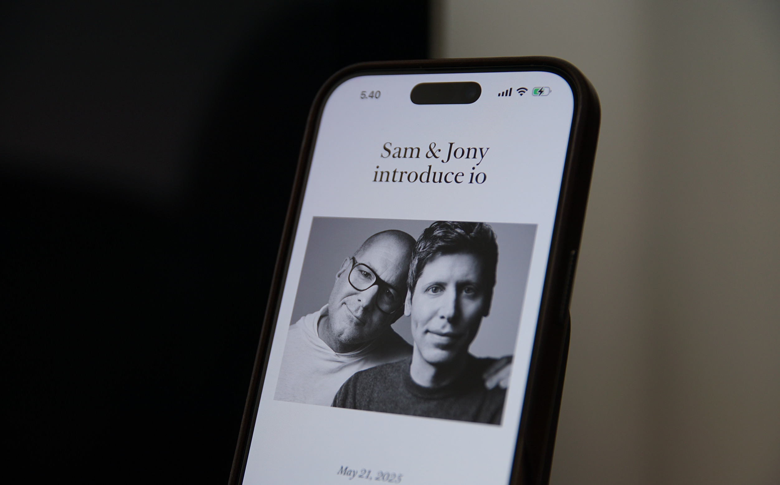 Das Bild zeigt einen Smartphone-Bildschirm mit dem Text "Sam & Jony introduce io" und einem schwarz-weißen Porträt von zwei Personen. Es ist der 21. Mai 2023 vermerkt. Die Darstellung wirkt modern und minimalistisch.