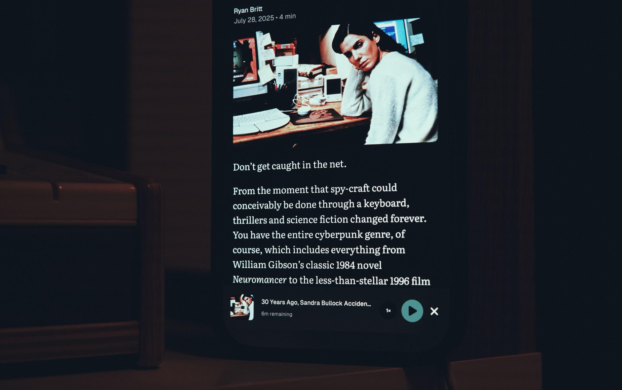A smartphone screen displaying an article featuring a black and white image of a woman leaning on a desk with a computer, in a room with scattered items and a keyboard. Text accompanying the image discusses cyberpunk themes, mentioning William Gibson's "Neuromancer" and a 1996 film. A circular play button and a close button are visible at the bottom of the screen.

