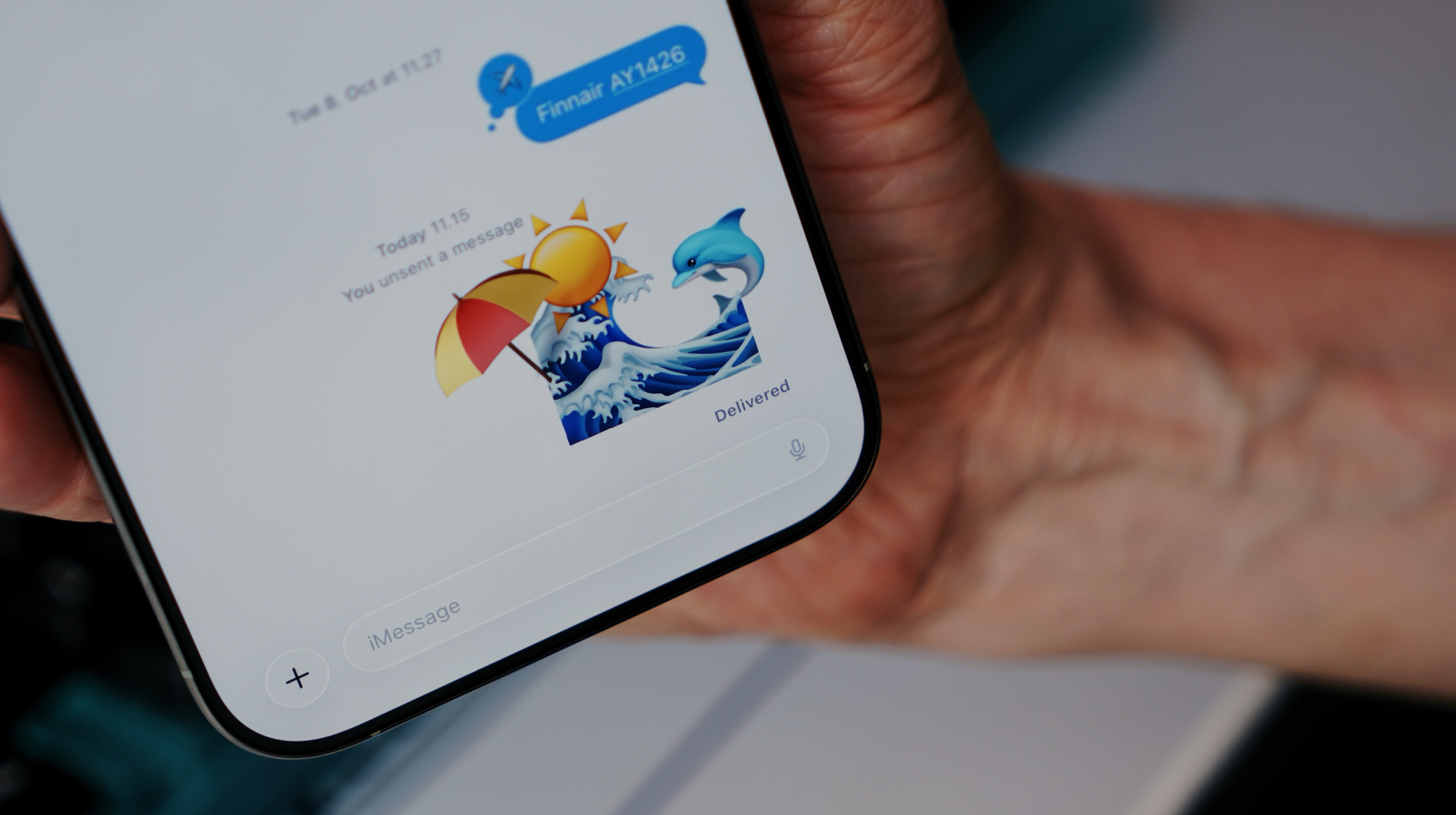 A hand holding a smartphone displaying an iMessage conversation with Finnair AY1426, including emojis of a sun with an umbrella, a wave, and a dolphin; the message "You unsent a message" is also visible.