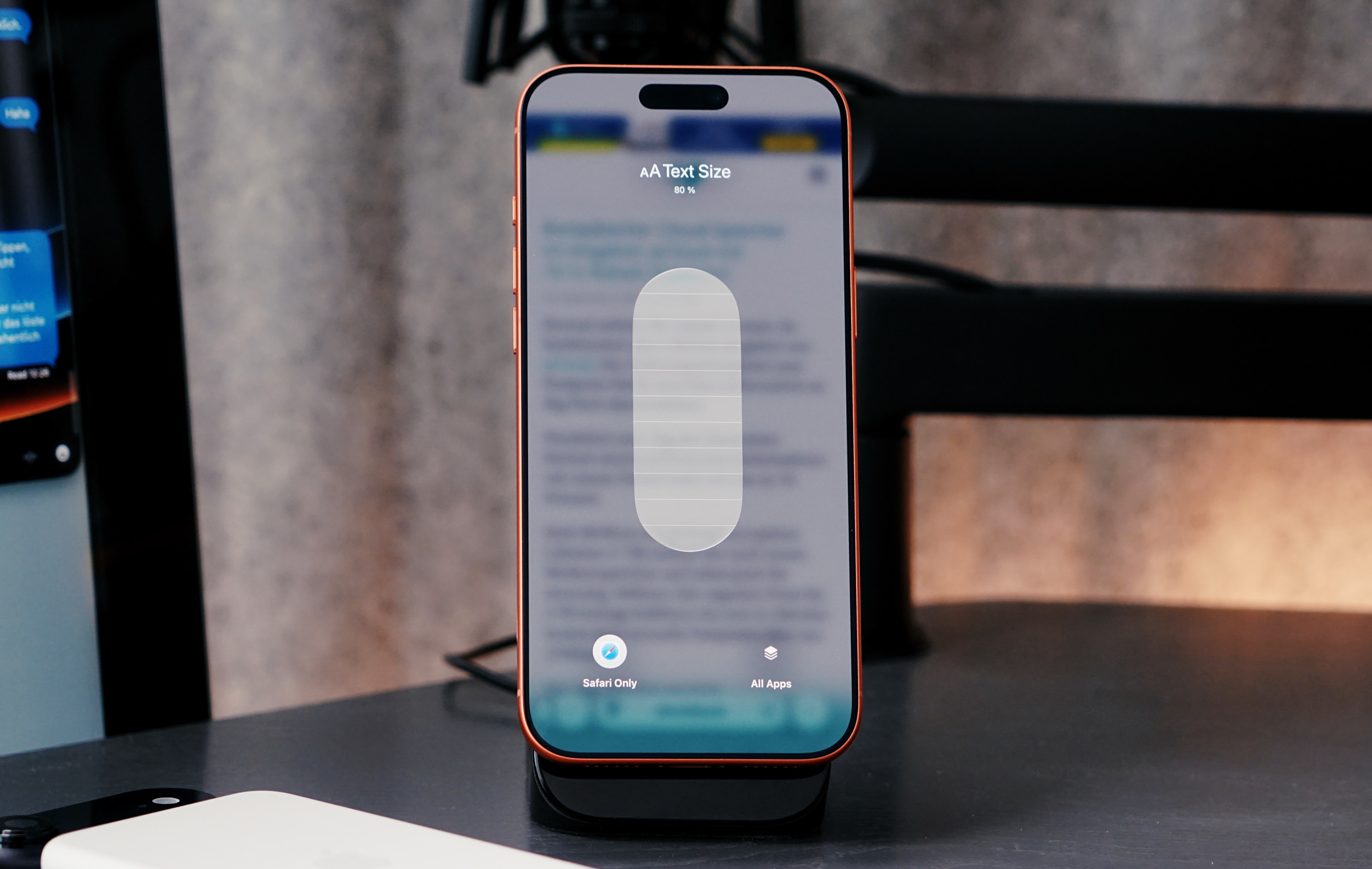 An iPhone displaying the text size control interface, with "AA Text Size 80%" and an adjustable slider, while on a wireless charging stand.
