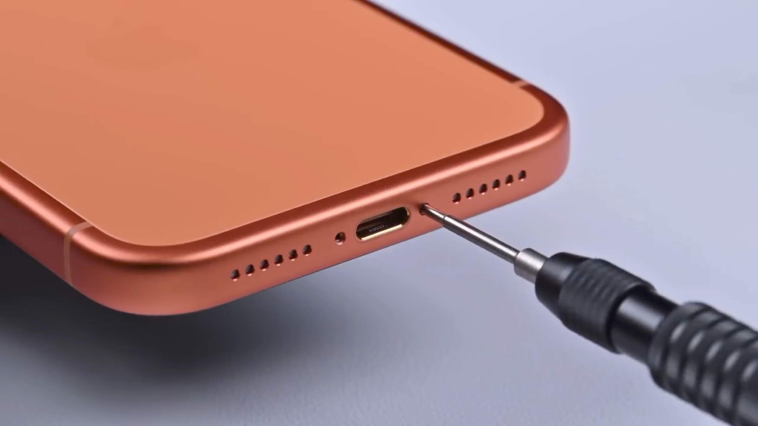 Close-up view of an orange-colored smartphone's bottom edge, with a small screwdriver inserting a screw into the phone's charging port area.
