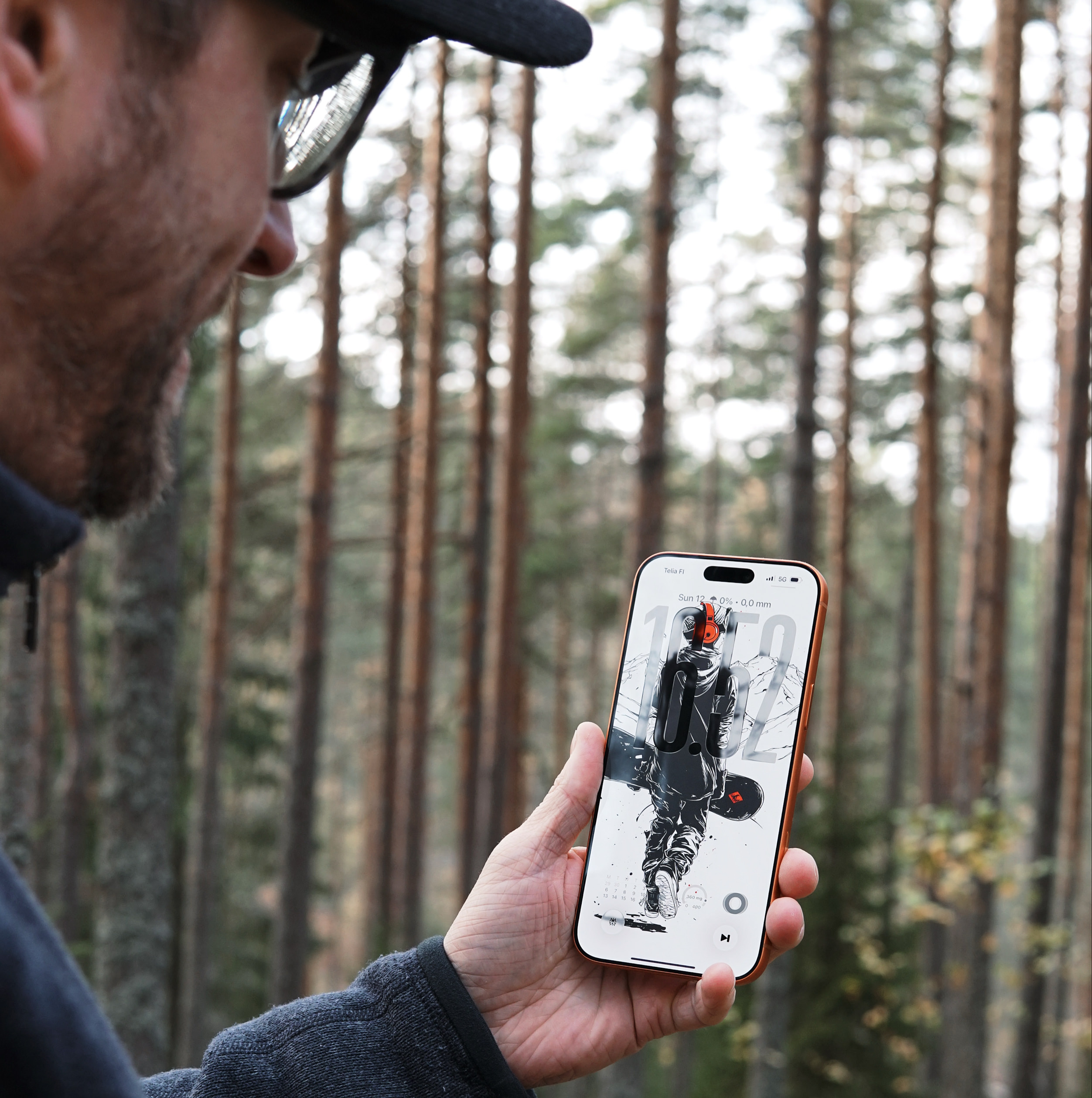 Man holding a smartphone with a wallpaper depicting an astronaut with a snowboard, in a forest setting.