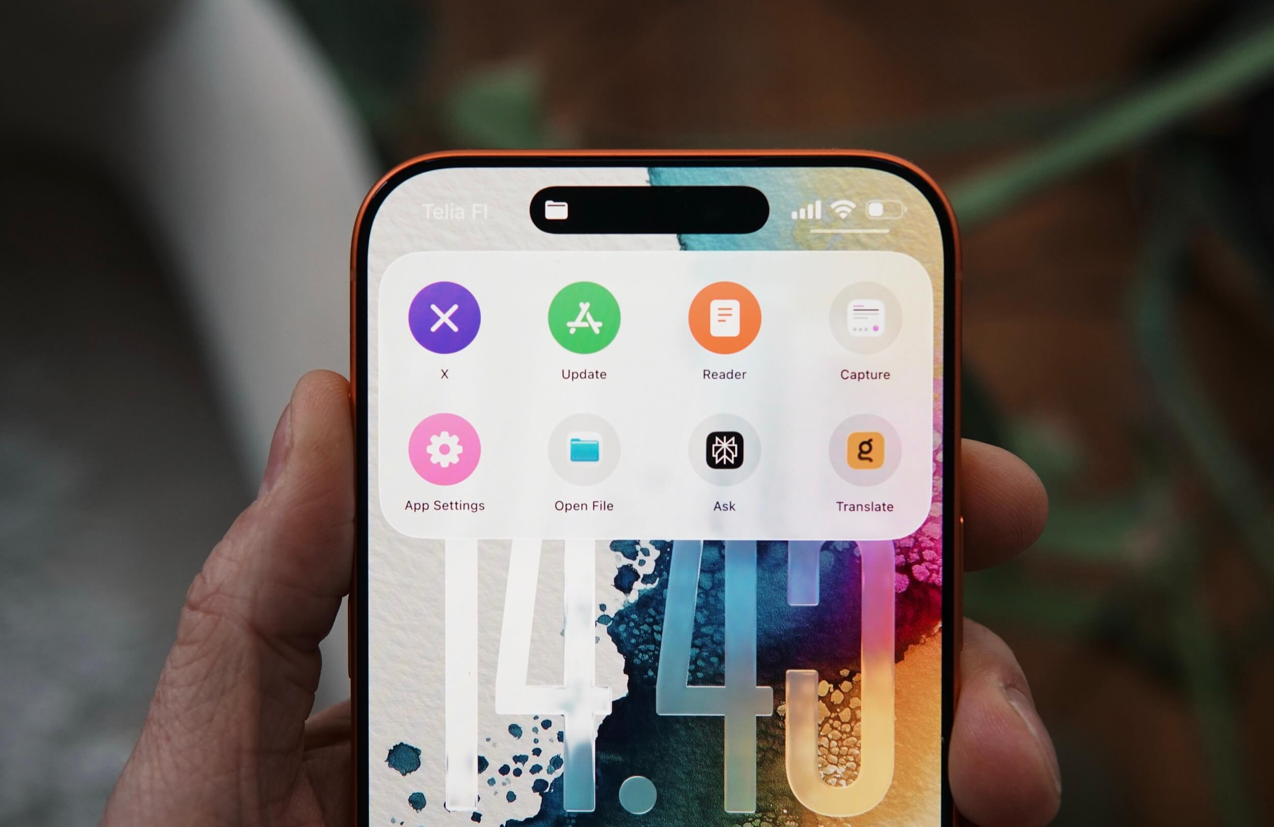 Hand holding a modern smartphone displaying a home screen with a selection of app icons, including X, Update, Reader, and App Settings, with time displayed as 14:40.
