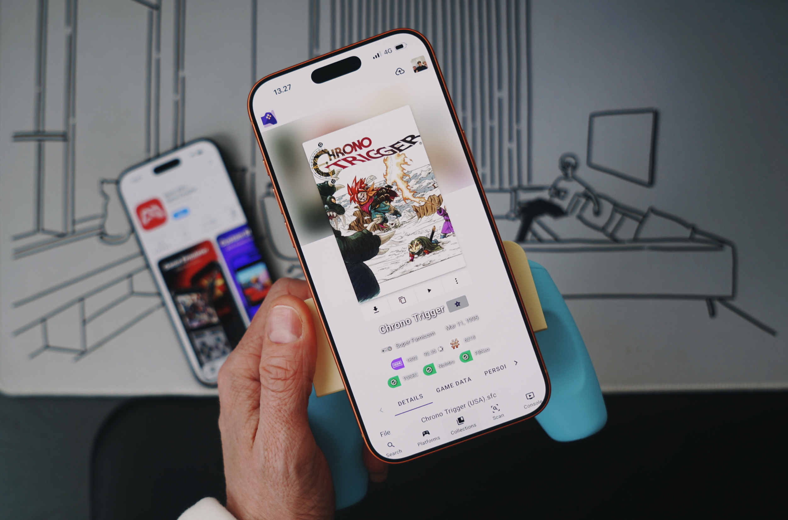 A hand holding an orange iPhone displaying the Chrono Trigger video game cover art on the screen. The phone displays game details, including "Chrono Trigger" title, release date, and Super Famicom platform information. Another phone is visible in the background, showing a mobile app interface. The background features abstract drawn elements.
