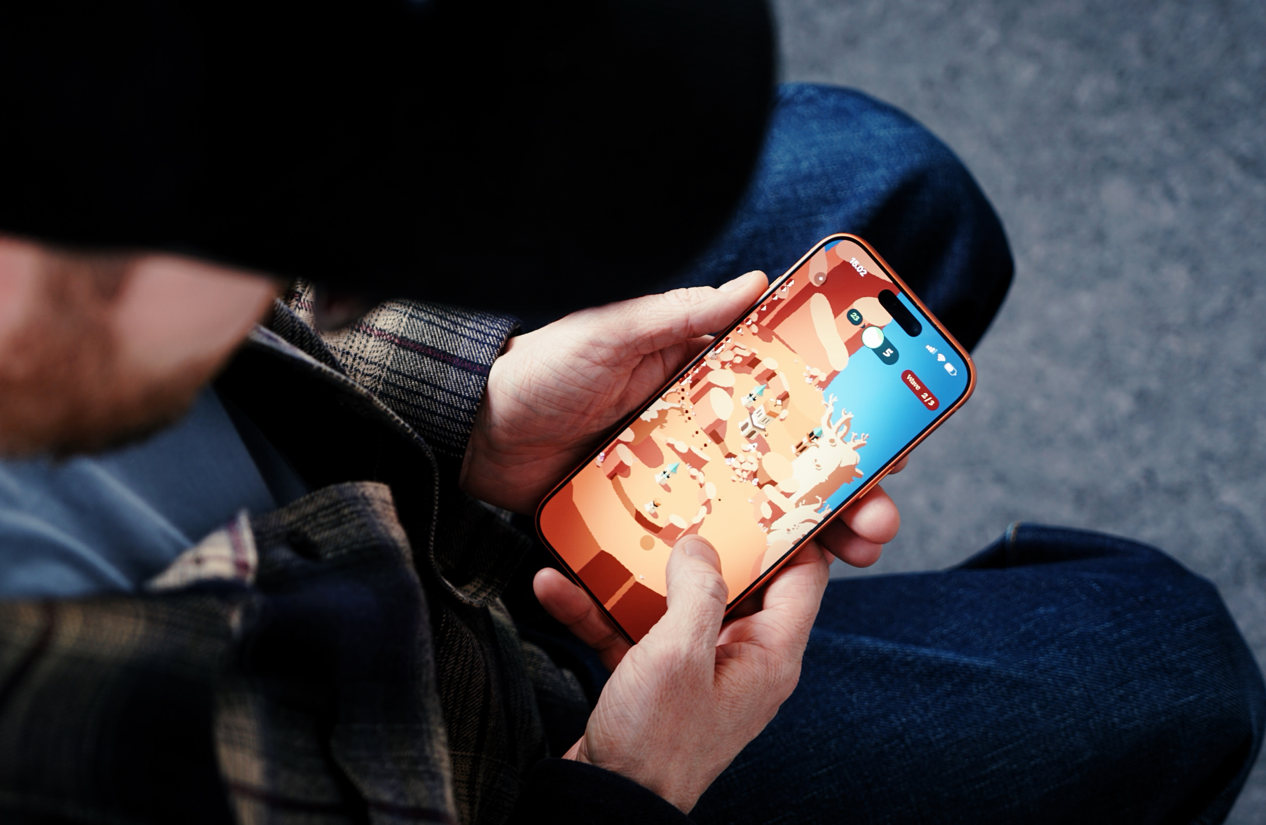 Person hält ein orangefarbenes Smartphone, das ein farbenfrohes, abstraktes Handyspiel auf blauem und orangefarbenem Hintergrund anzeigt, vor einem verschwommenen Hintergrund aus Torso und Beinen einer Person.
