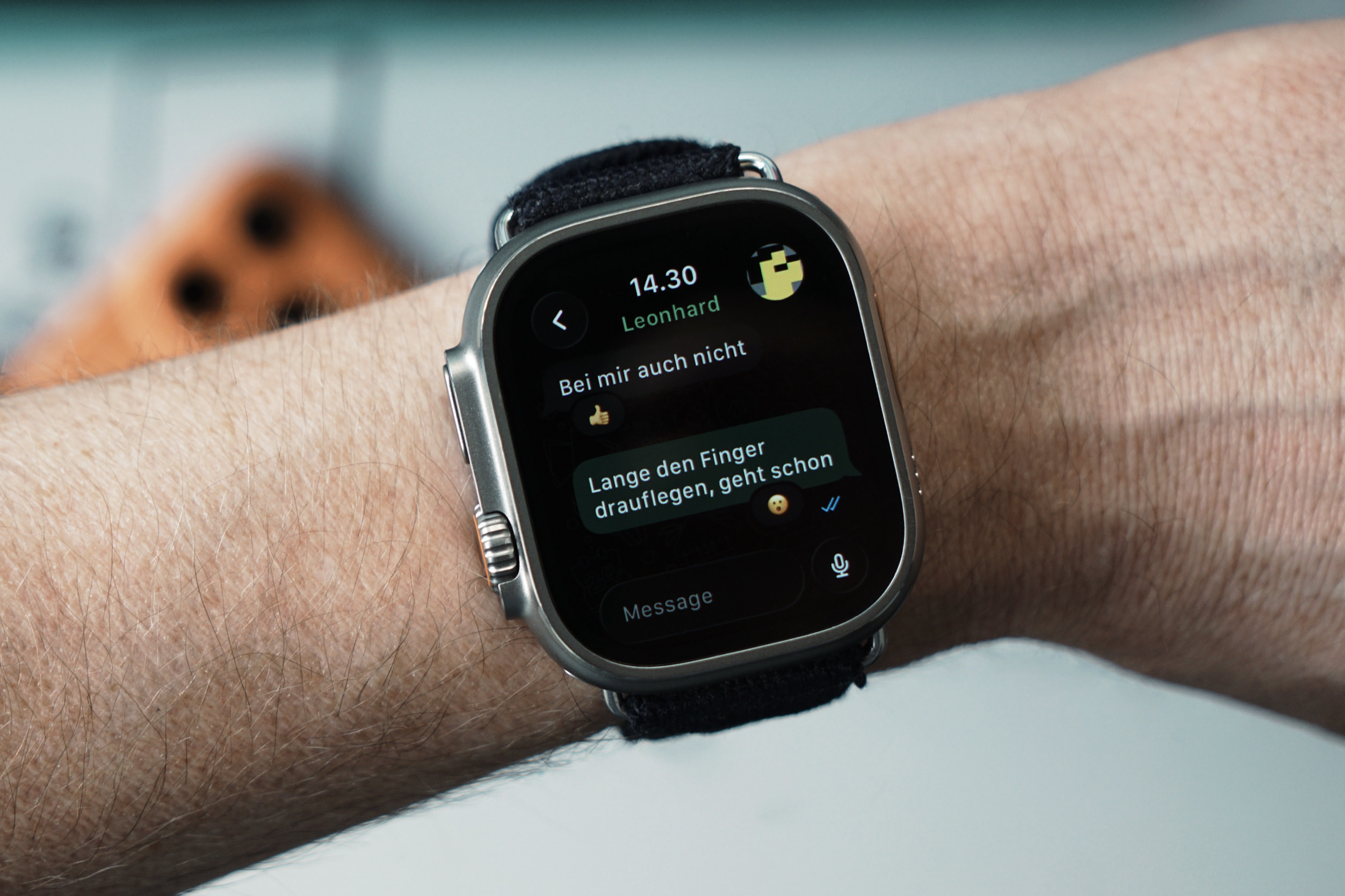 A close-up of a wrist with a silver smartwatch displaying a messaging app. The time on the watch reads "14.30" and the sender is "Leonhard." The message threads say: "Bei mir auch nicht" and "Lange den Finger drauflegen, geht schon."
