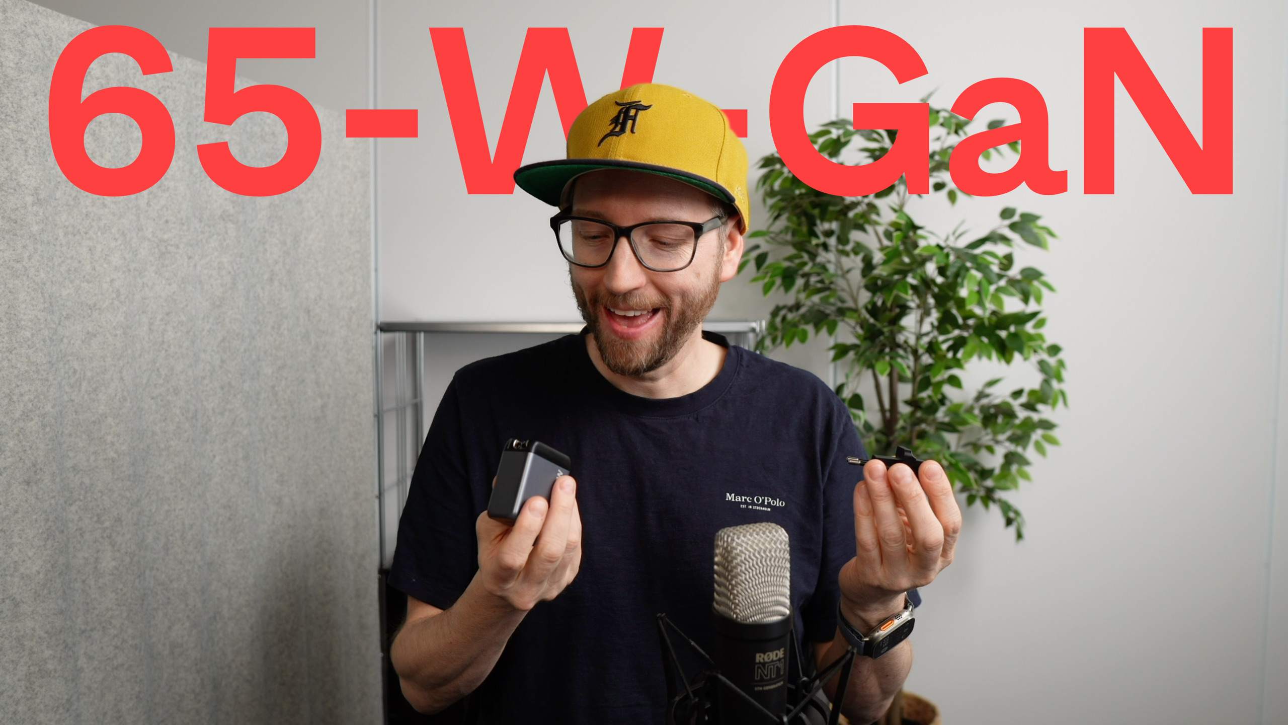 Ein Mann mit Baseballkappe hält ein kleines Ladegerät in seinen Händen, mit "65-W-GaN" in roten Buchstaben oben.