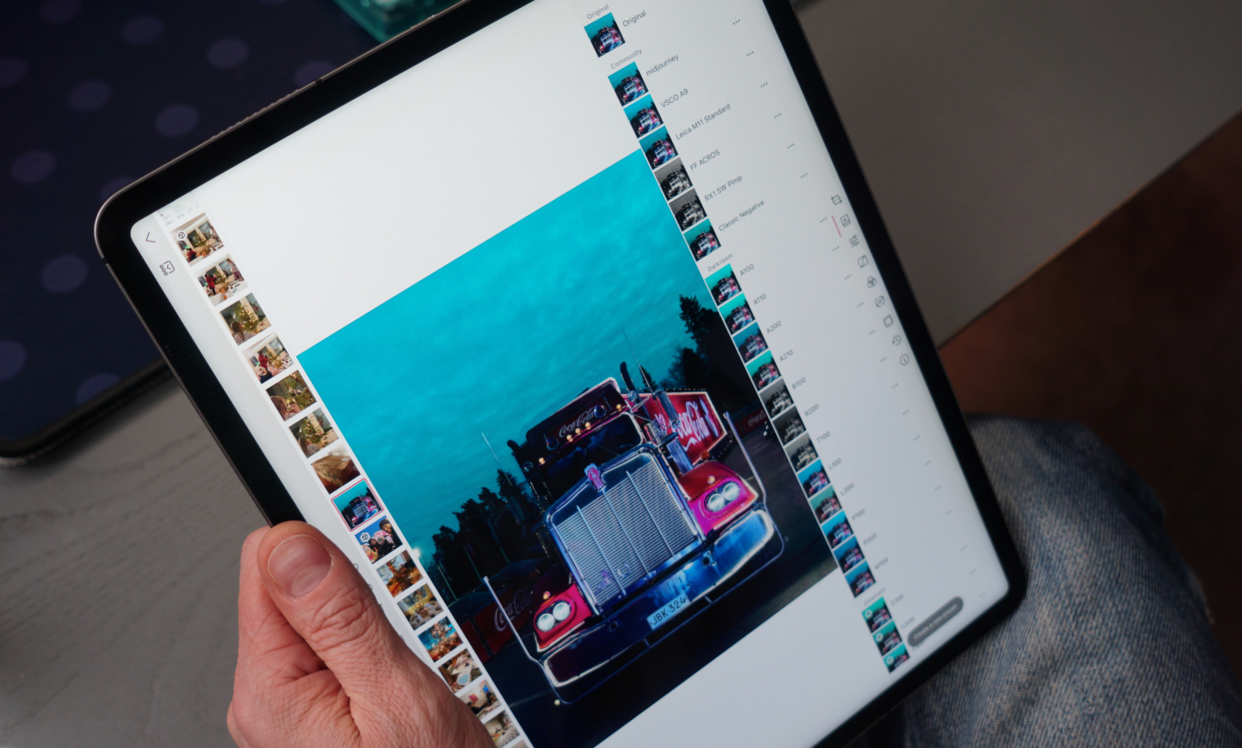 A hand holding a tablet displays an edited image of a red semi-truck with a Coca-Cola sign in front of a blue sky, within an editing application interface featuring a list of preset filters.

German:
Eine Hand, die ein Tablet hält, zeigt ein bearbeitetes Bild eines roten Sattelschleppers mit einem Coca-Cola-Schild vor einem blauen Himmel, in einer Bearbeitungsanwendungsoberfläche mit einer Liste von Voreinstellungen.
