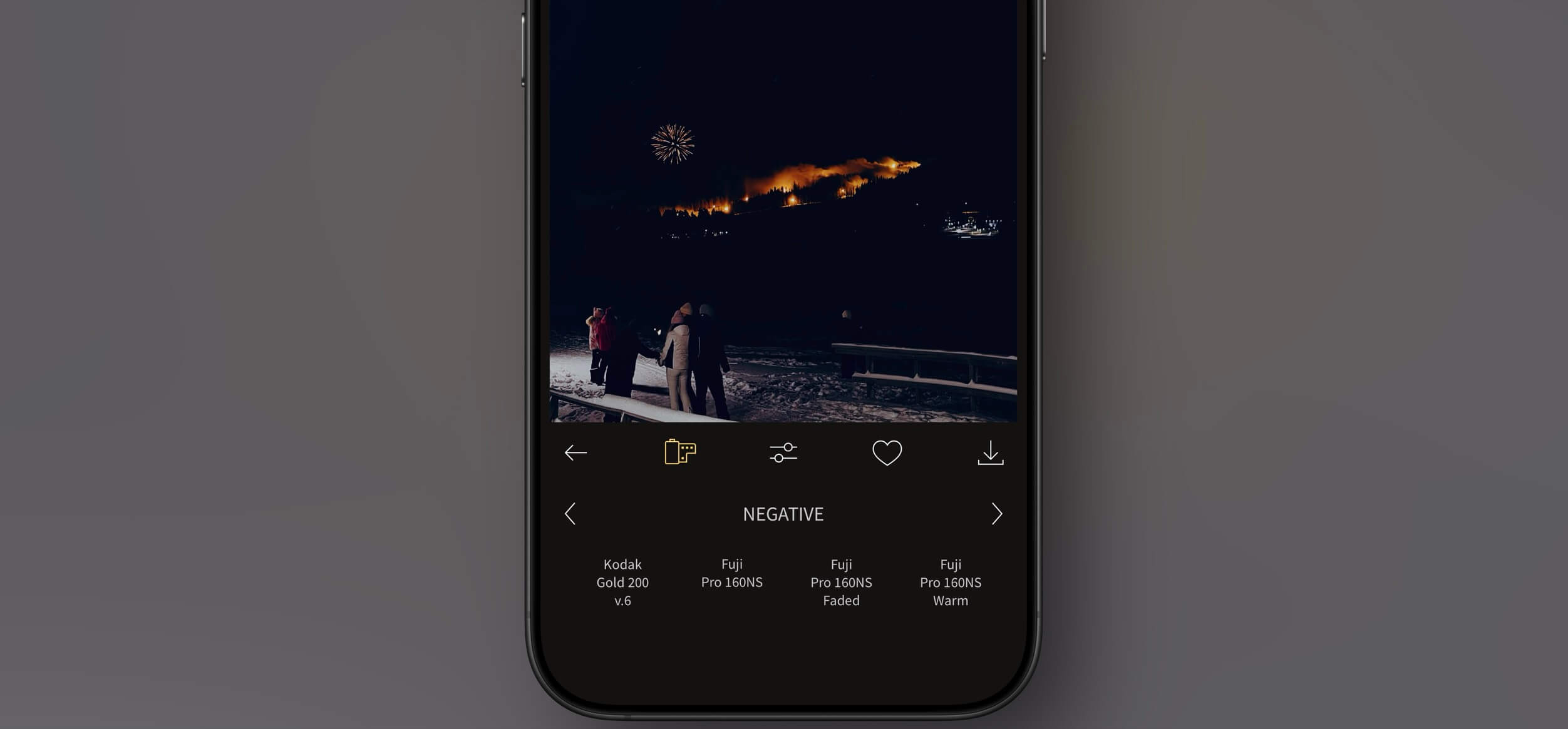 Smartphone screen displaying photo editing app interface, with a night scene of fireworks, people, and a snowy landscape. The app's filter options are displayed below, under the "NEGATIVE" category.
