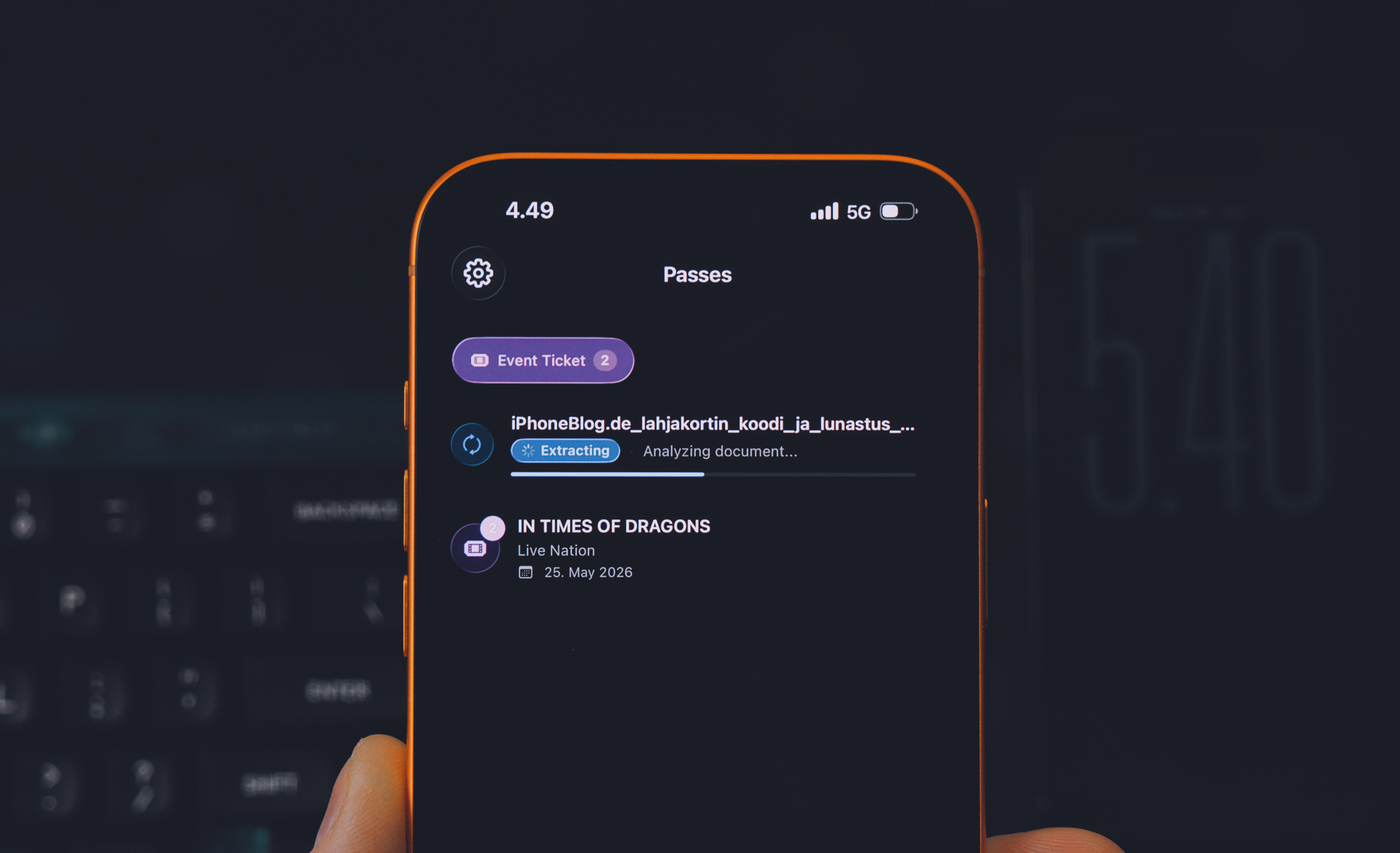 Eine Person, die ein orangefarben umrandetes Smartphone hält, das einen "Pässe"-Bildschirm mit Event-Tickets anzeigt. Das Telefon zeigt Event-Details für "IN TIMES OF DRAGONS" und ein weiteres Ticket an, das gerade Daten extrahiert. Die Uhrzeit 4.49 und 5G-Konnektivität werden ebenfalls angezeigt.
