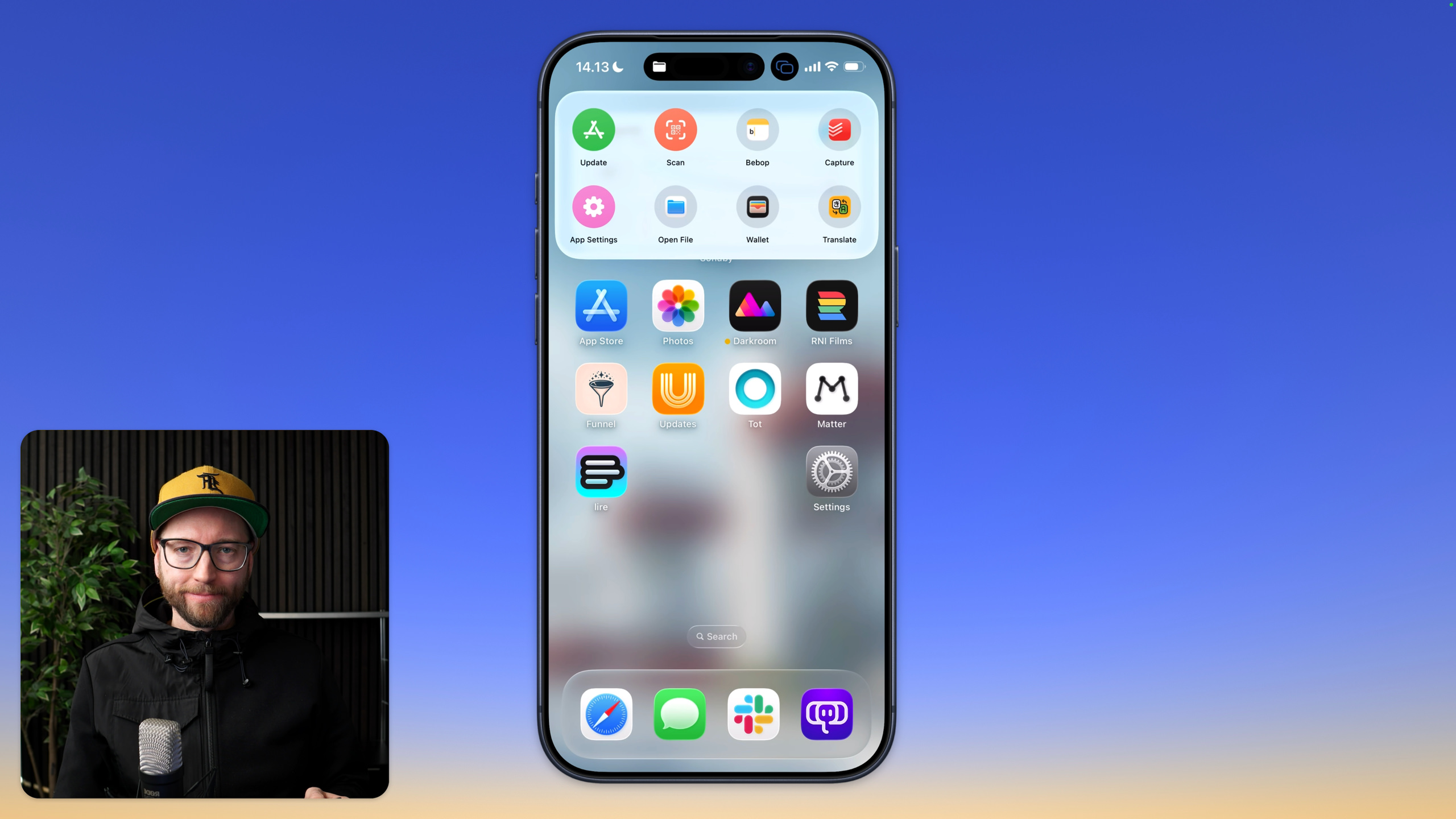 
Ein Mann mit Brille, Hut und schwarzer Jacke befindet sich auf der linken Seite des Bildes und hält ein Mikrofon. Auf der rechten Seite des Bildes zeigt ein Smartphone-Bildschirm seinen Startbildschirm mit mehreren App-Symbolen, darunter Symbole für „Update“, „Scan“, „Bebop“, „Capture“, „App-Einstellungen“, „Datei öffnen“, „Wallet“, „Übersetzen“, „App Store“, „Fotos“, „Darkroom“, „RNI Films“, „Funnel“, „Updates“, „Tot“, „Matter“, „lire“, „Einstellungen“ und eine Suchleiste.
