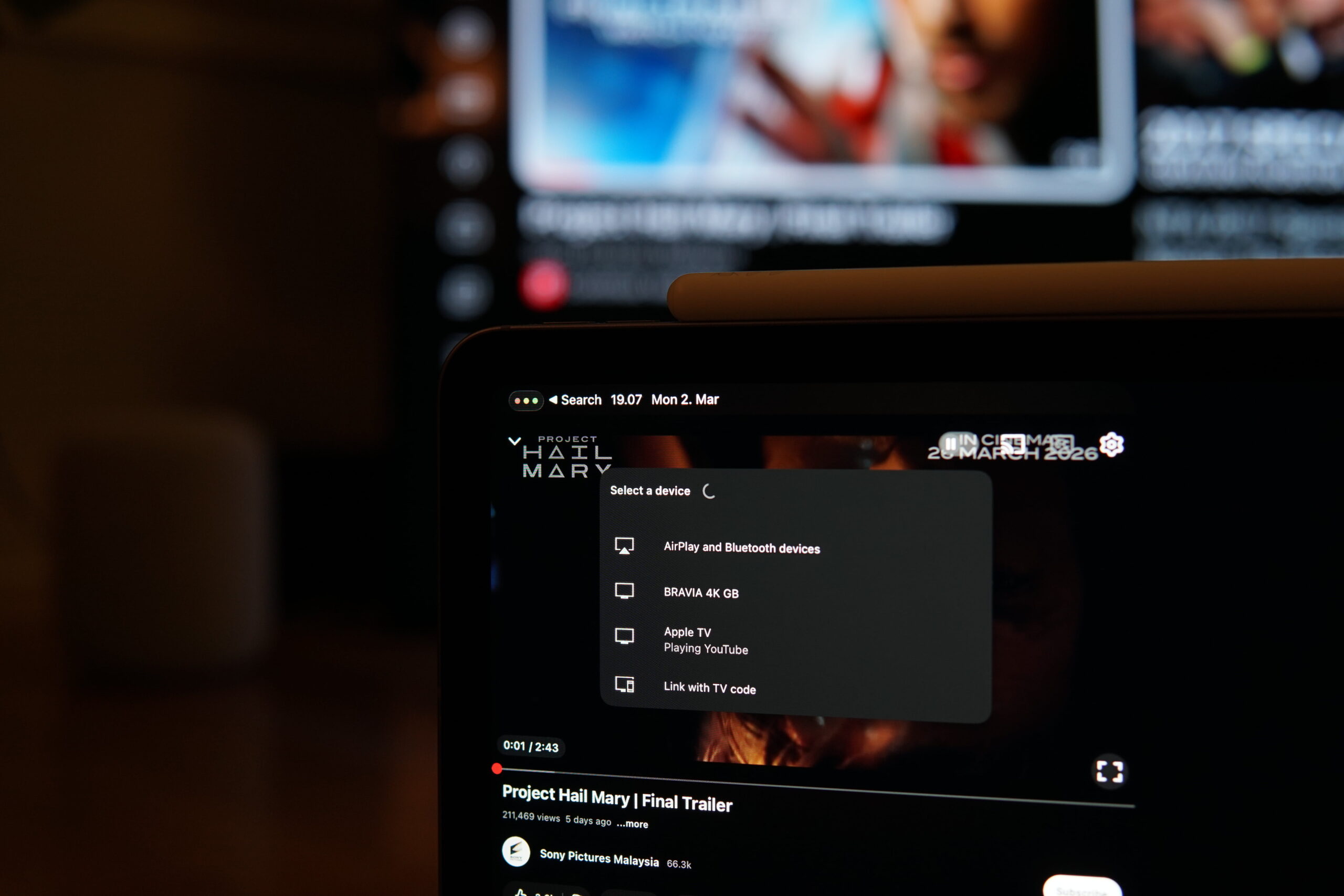 Ein Tablet-Bildschirm, auf dem ein YouTube-Video für "Project Hail Mary | Final Trailer" angezeigt wird. Das Tablet zeigt Optionen zur Auswahl eines Geräts an, darunter "AirPlay und Bluetooth-Geräte", "BRAVIA 4K GB", "Apple TV" und "Mit TV-Code verknüpfen". Über dem Video steht "IN CISTEMAR 26. MÄRZ 2026". Die Uhrzeit in der oberen linken Ecke lautet "19:07 Mo. 2. Mar". Im Hintergrund ist ein Fernsehbildschirm verschwommen.
