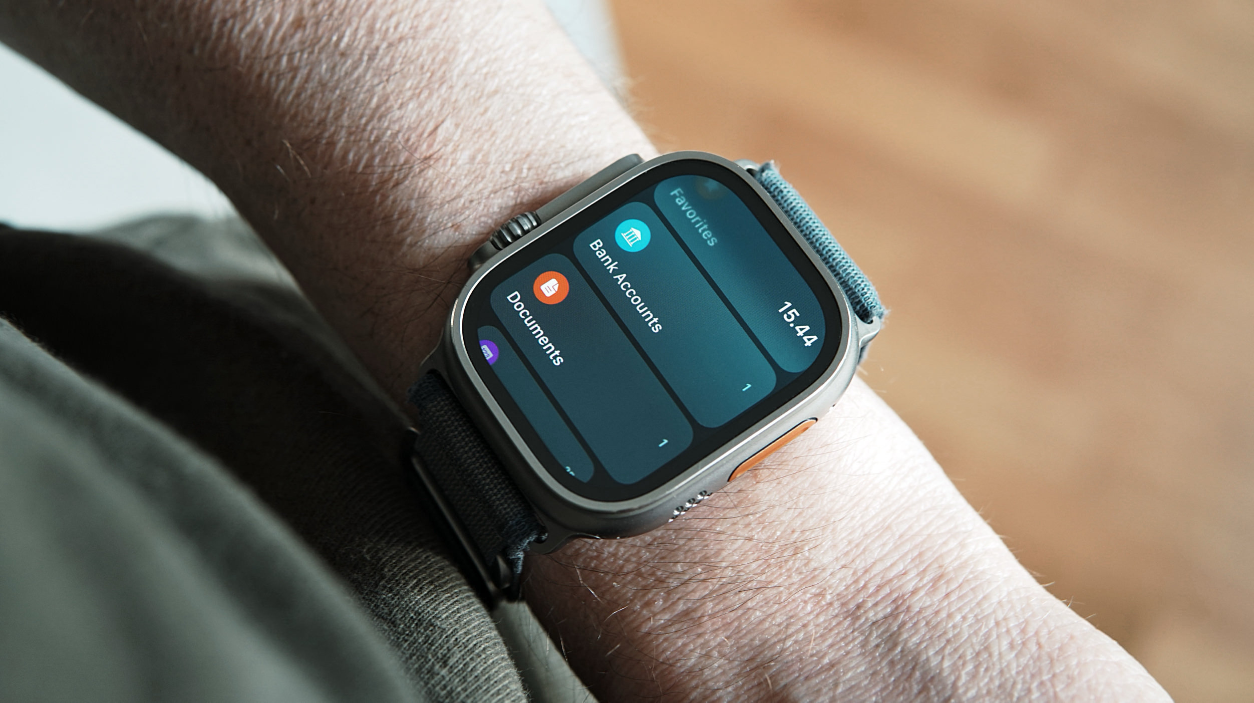 Das Handgelenk einer Person mit einer Apple Watch Ultra, die ein Menü mit den Optionen "Favoriten", "Bankkonten" und "Dokumente" anzeigt. Die Uhrzeit 15:44 ist ebenfalls sichtbar.