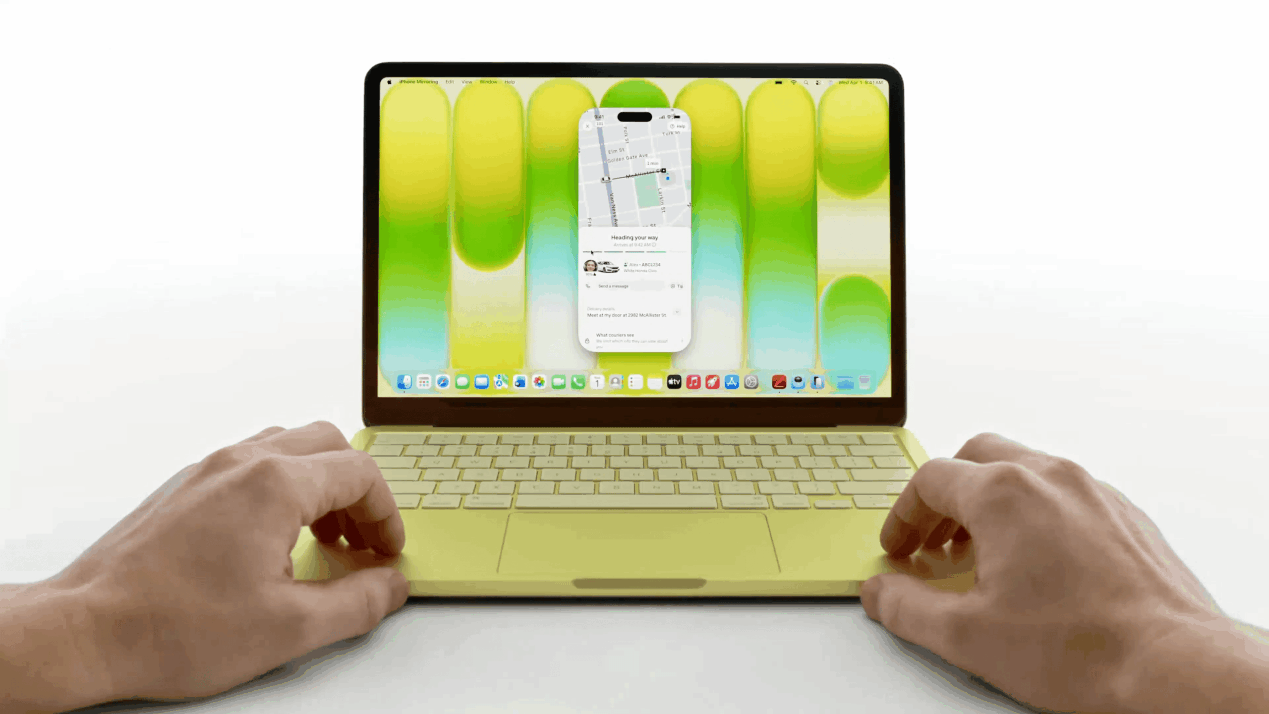 Ein gelber Laptop ist geöffnet und spiegelt die Anzeige eines Smartphones auf seinem Bildschirm wider. Auf dem Bildschirm ist eine Navigations-App mit dem Text "Unterwegs", zusammen mit einem Autosymbol und dem Namen "Alex ABC1234" zu sehen. Die Tastatur des Laptops ist im Fokus, mit zwei Händen, die sich in der Nähe des Trackpads befinden.