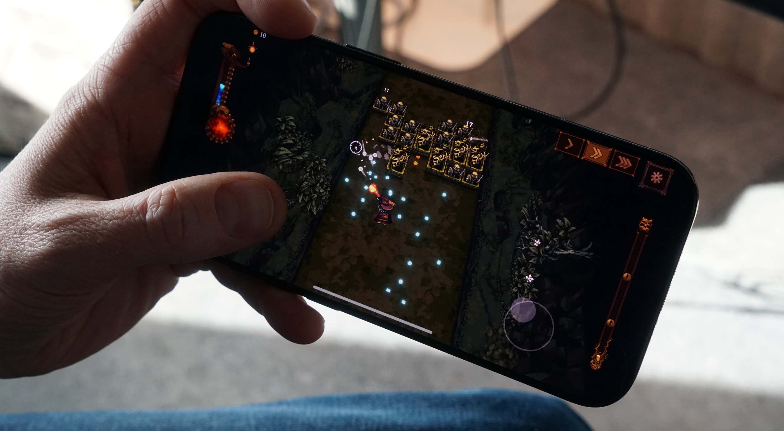 Hand hält ein Smartphone, das ein Handyspiel anzeigt. Das Spiel ist eine Draufsicht auf eine verpixelte Kampfszene mit einem Charakter, der Feinde bekämpft. In der oberen linken Ecke steht "10" und über den Feinden steht "17".