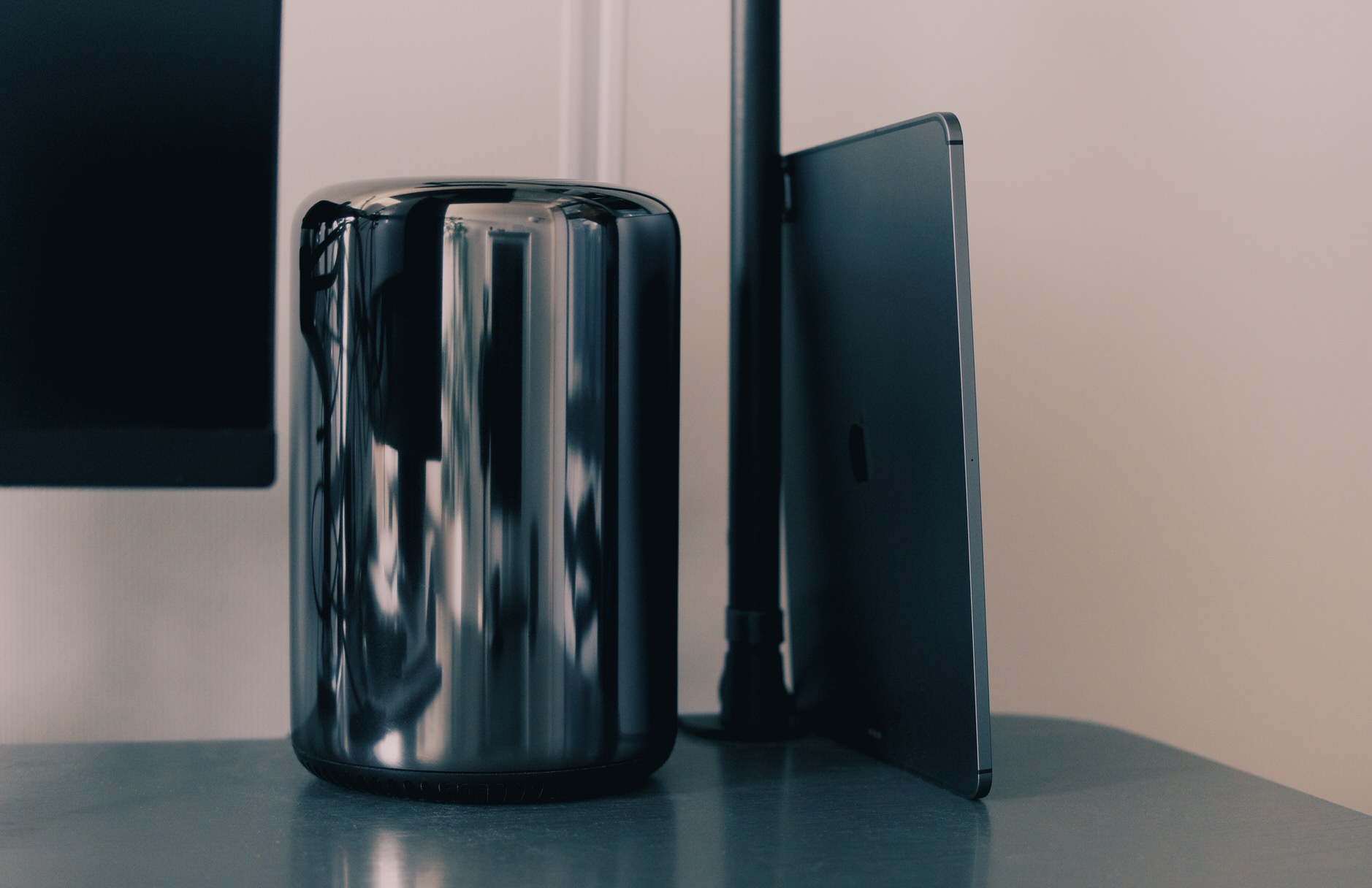 Ein glänzender, schwarzer, zylindrischer Desktop-Computer – MacPro – steht auf einem Schreibtisch neben einem dünnen, dunklen, rechteckigen Tablet (iPad), das an einem Monitorarm angelehnt ist.