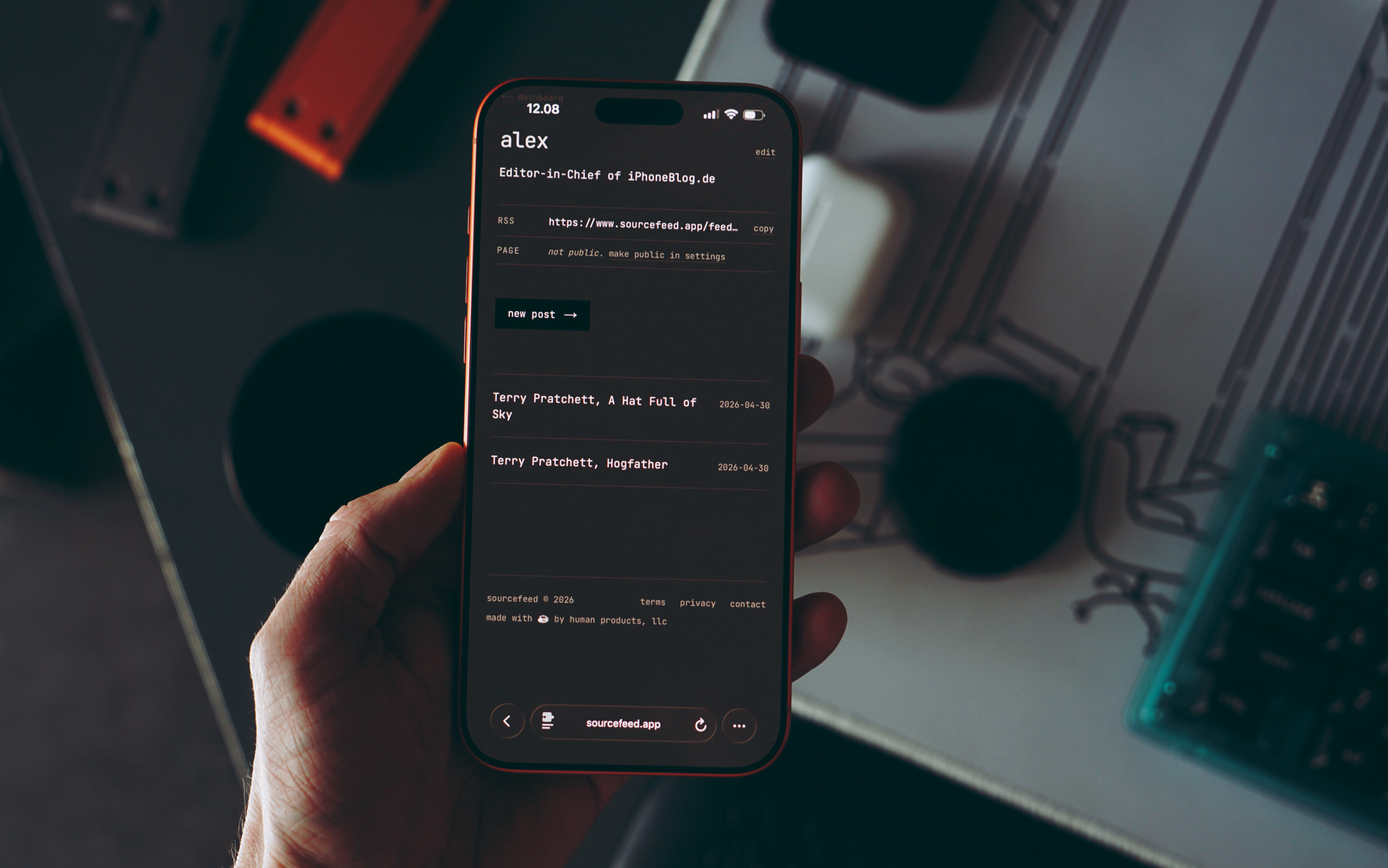 Eine Hand hält ein Smartphone, das die Benutzeroberfläche der App „sourcefeed.app“ in einem dunklen Design anzeigt.