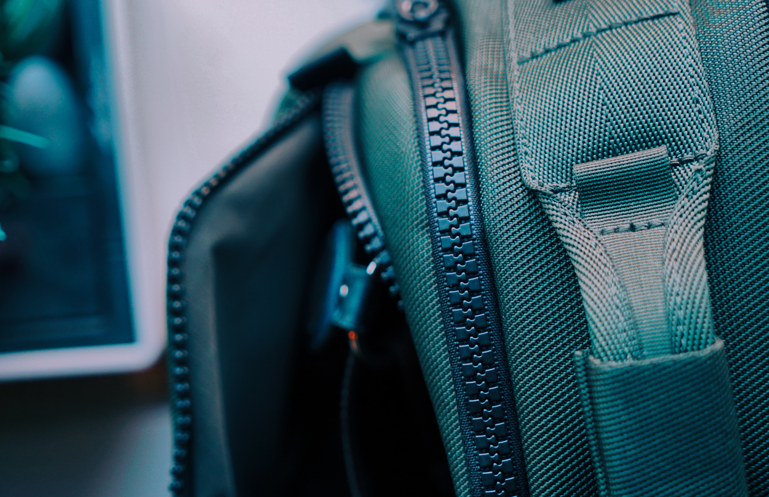 Nahaufnahme eines dunkelgrünen Rucksacks aus strukturiertem Stoff, mit Fokus auf den robusten Reißverschluss und einen verstärkten Tragegriff.