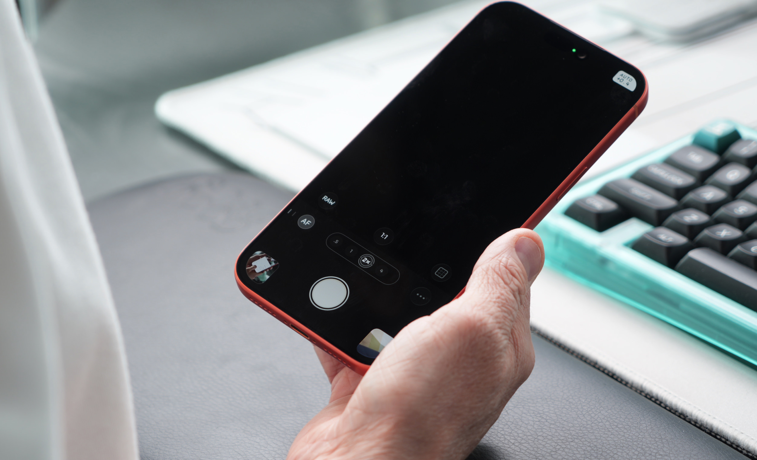 Eine Hand hält ein rotes Smartphone, auf dessen Bildschirm die Benutzeroberfläche der Kamera-App angezeigt wird.