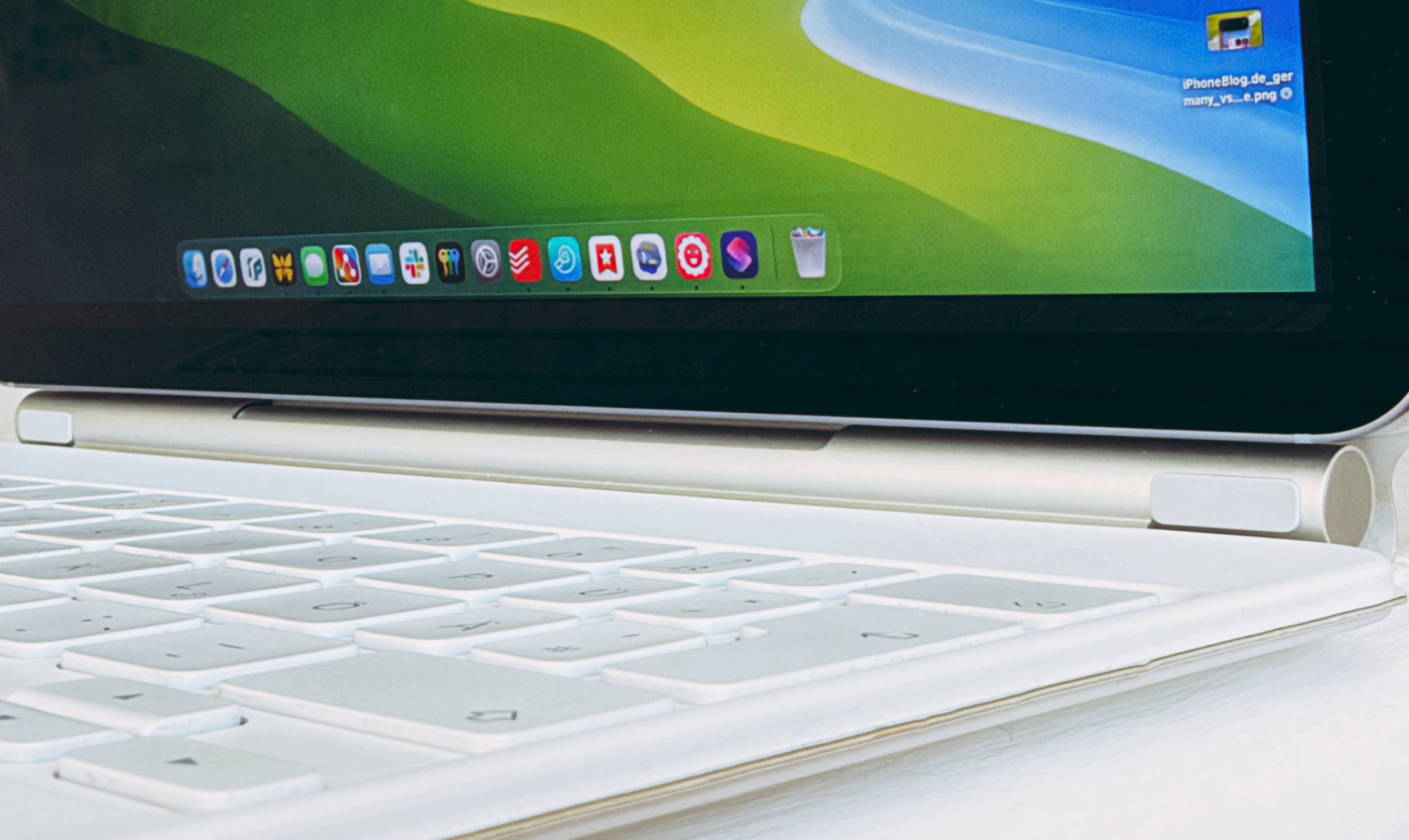 Nahaufnahme einer weißen Tastatur, die mit einem Tablet oder Laptop verbunden ist, wobei auf dem Bildschirm eine Taskleiste mit mehreren bunten Anwendungssymbolen zu sehen ist.