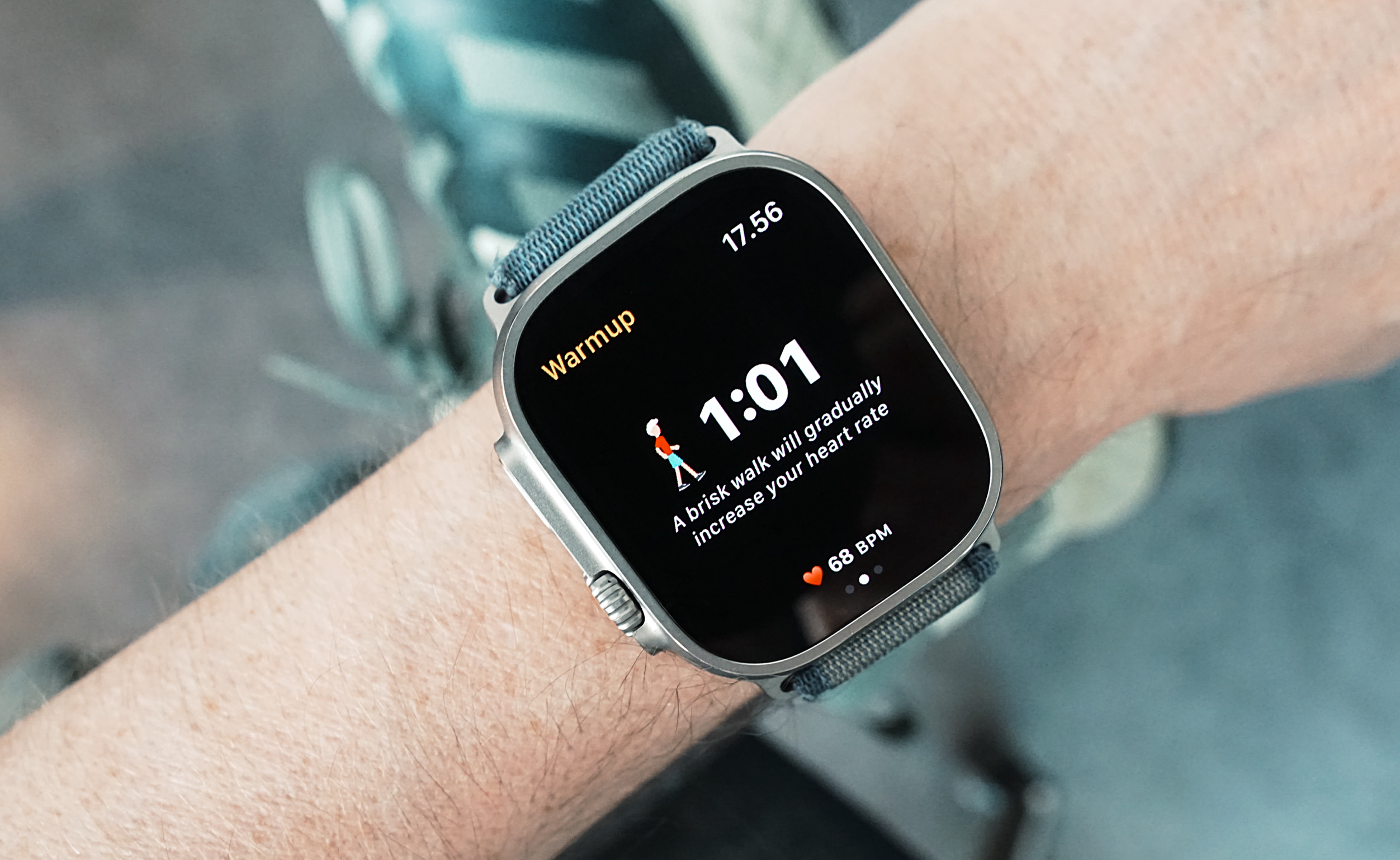 Nahaufnahme einer Smartwatch am Handgelenk einer Person, die einen Trainings-Aufwärmbildschirm mit Timer, Herzfrequenz und der Anweisung für ein zügiges Gehen anzeigt.