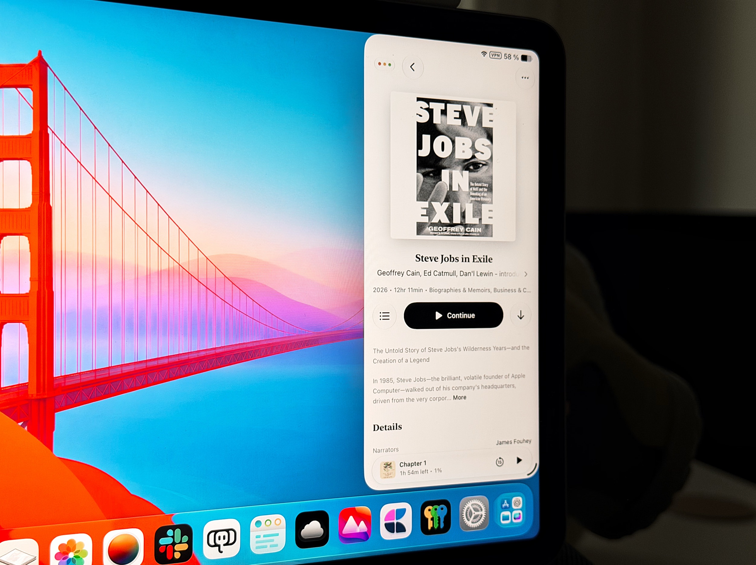A iPad screen displays the audiobook 'Steve Jobs in Exile' by Geoffrey Cain, with a 'Continue' button visible. The background wallpaper features the Golden Gate Bridge against a vibrant blue and pink sky.