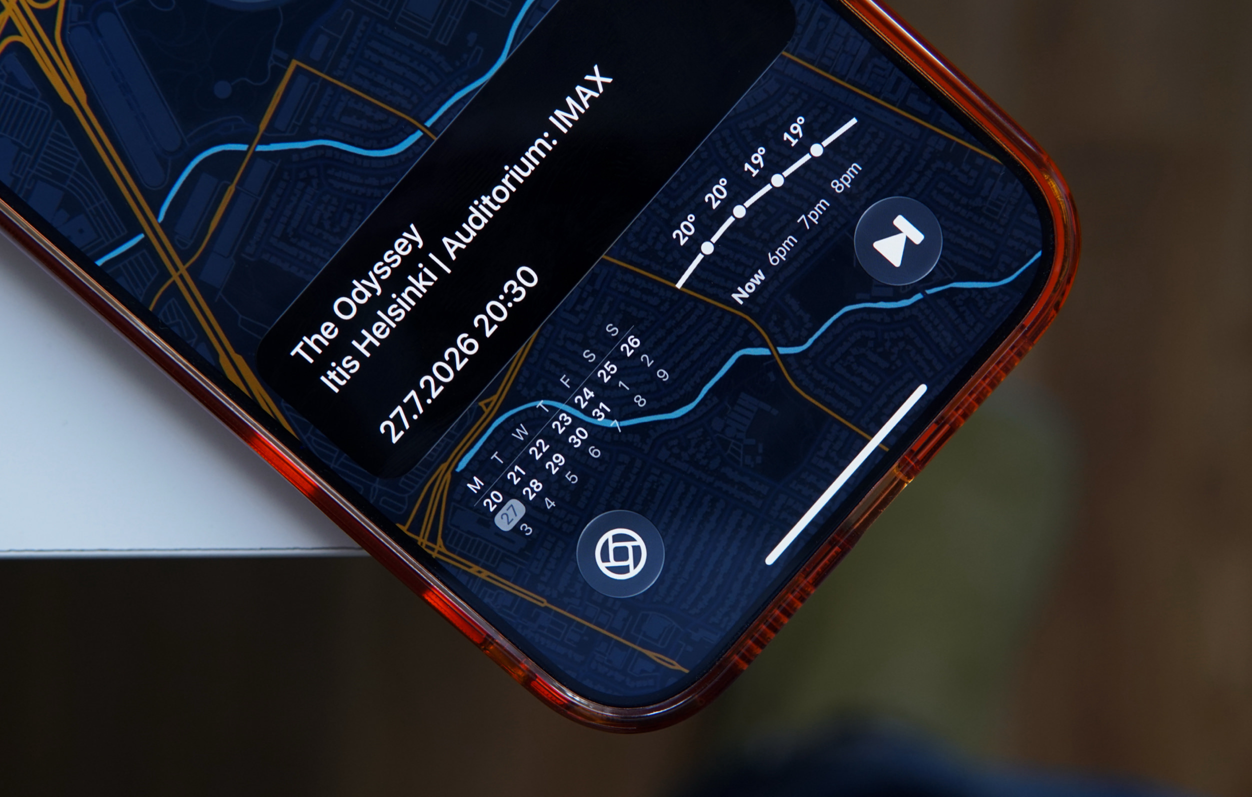 Nahaufnahme eines Smartphone-Bildschirms, der eine Benutzeroberfläche im Dark Mode zeigt, mit Widgets für Filminformationen, eine Wettervorhersage und einen Kalender, eingeblendet über einem Kartenhintergrund.