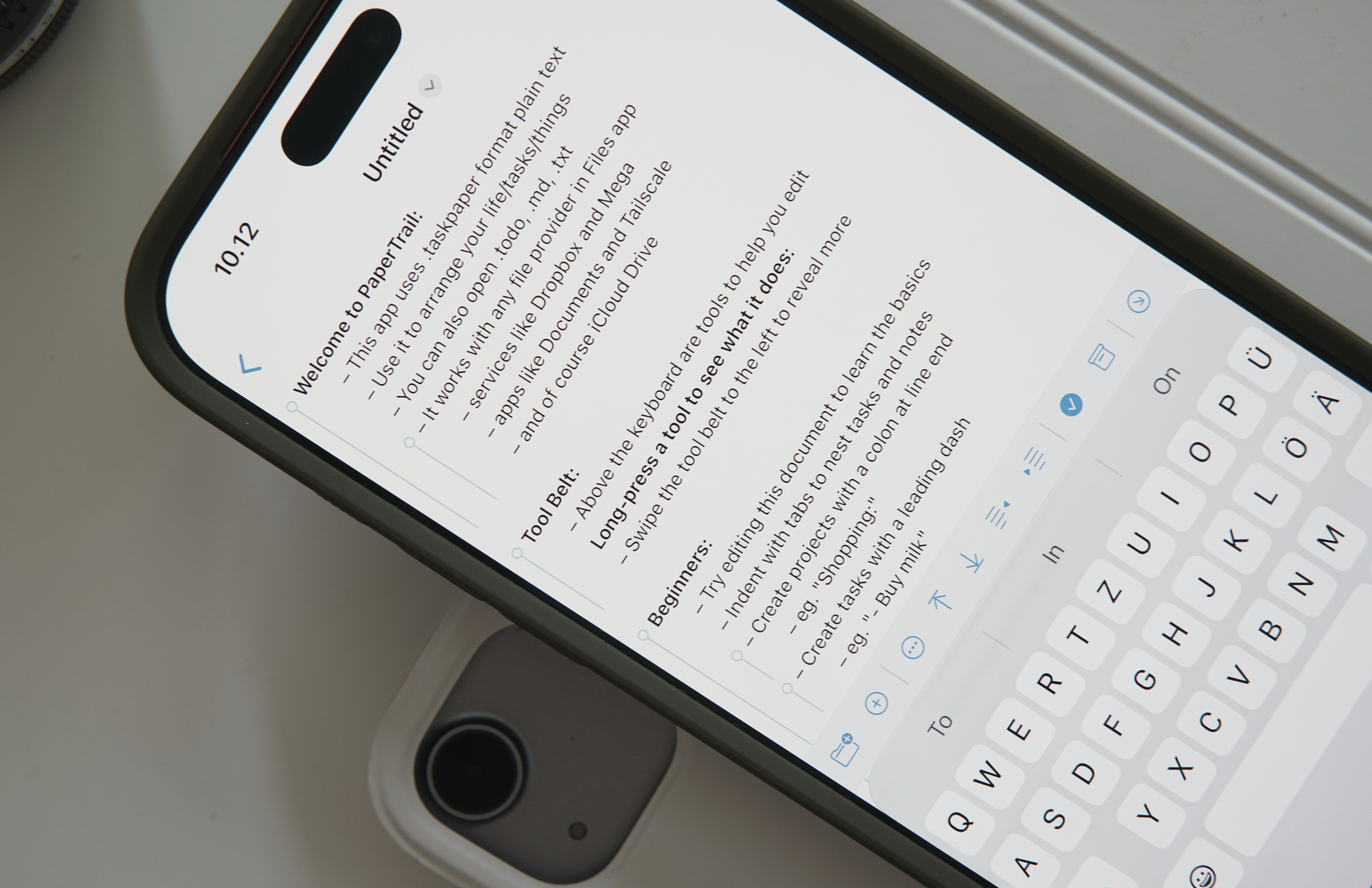 Eine Nahaufnahme eines Smartphone-Bildschirms, auf dem die App „PaperTrail“ geöffnet ist. Das Display zeigt eine Willkommensnachricht und Anweisungen zur Verwendung der App für die Organisation von Aufgaben und Notizen im Klartextformat. Am unteren Bildschirmrand ist eine virtuelle Tastatur zu sehen.