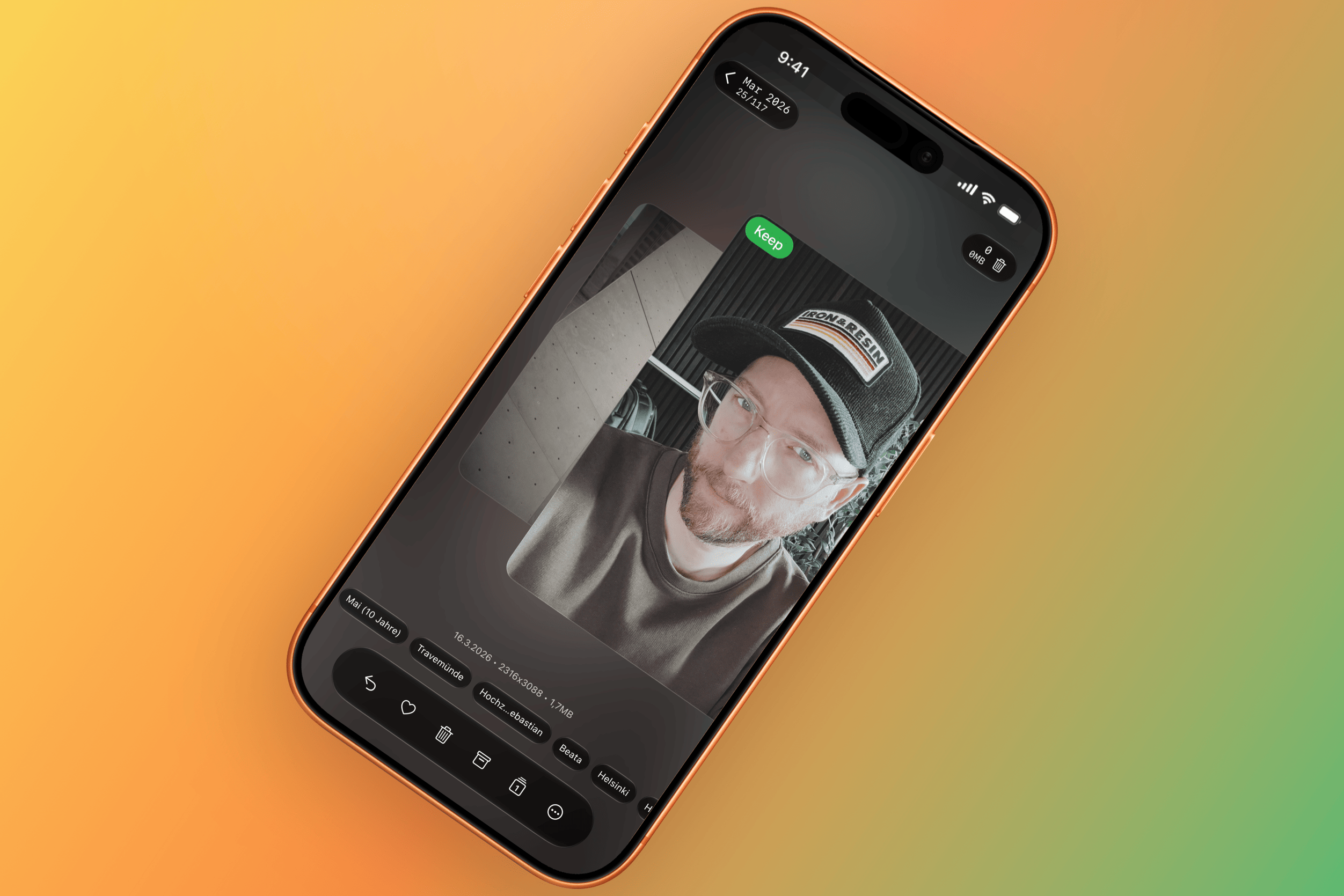 Ein Smartphone-Bildschirm zeigt eine App zur Fotoverwaltung. Zu sehen ist ein schwarz-weißes Selfie einer Person mit Brille und Baseballkappe, umgeben von verschiedenen App-Bedienelementen, Metadaten und Schlagworten.